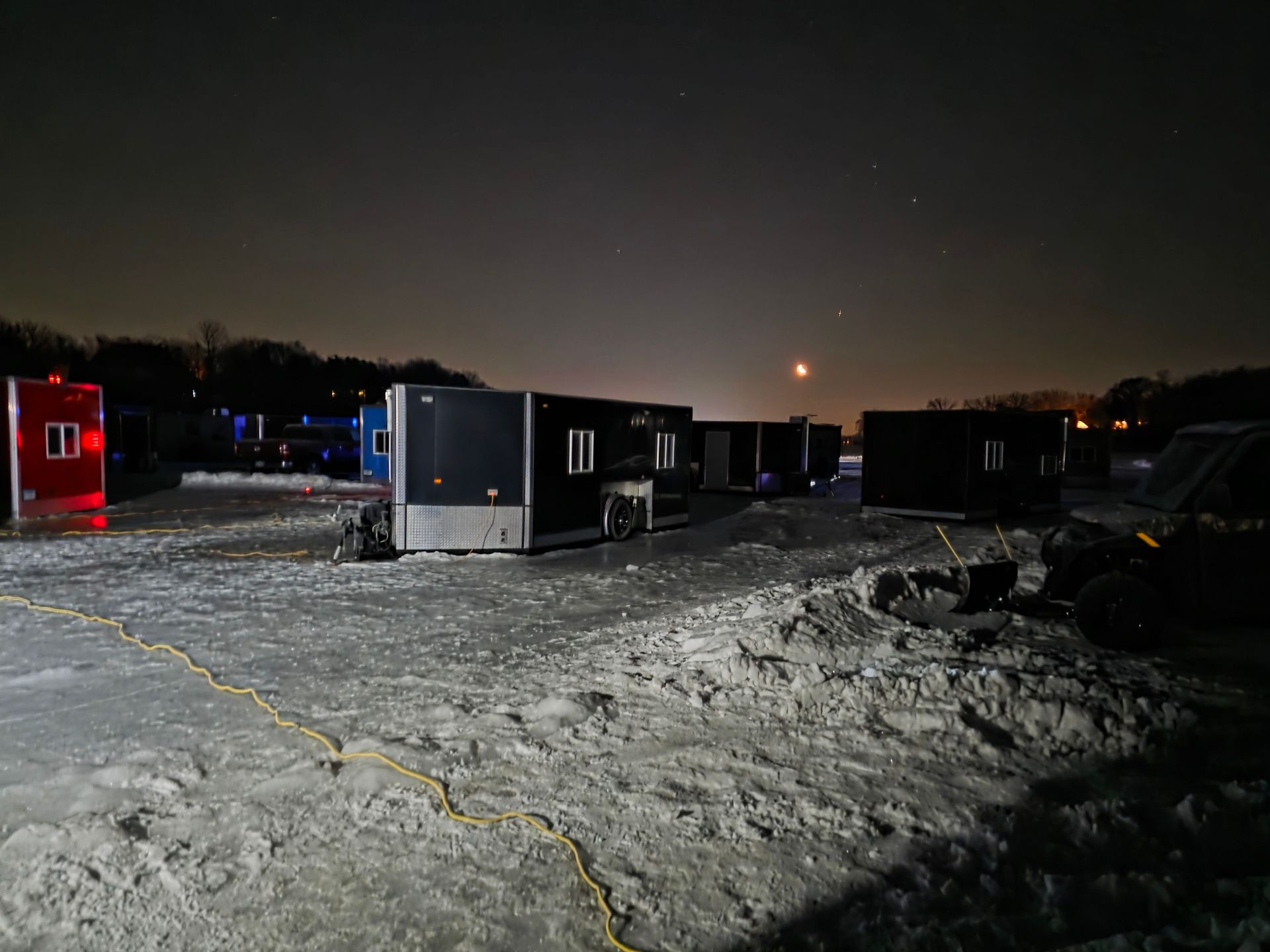 Snowy parking lot with dark trailers under a night sky and distant lights