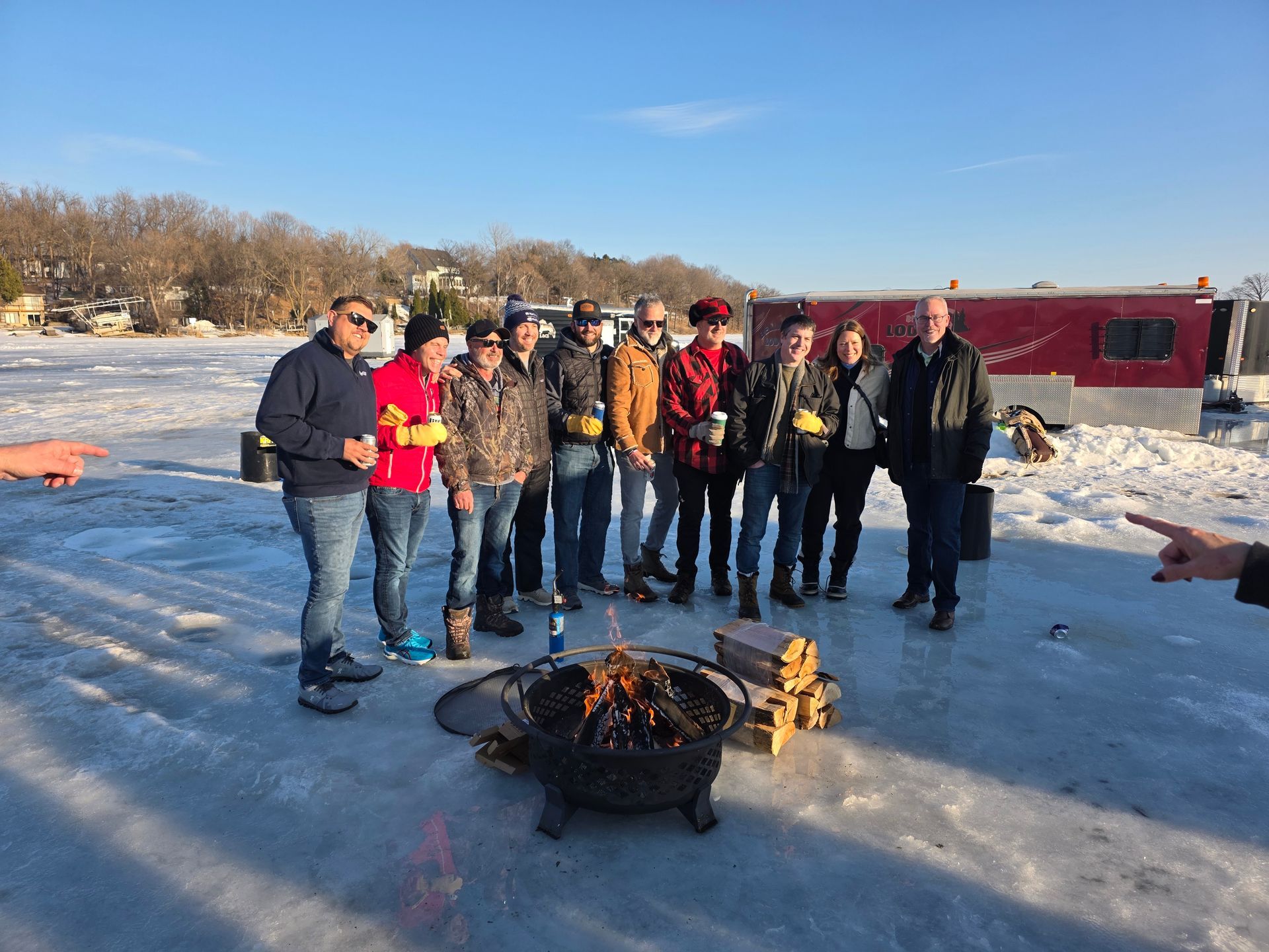 People standing around a fire pit on a frozen lake near red ice-fishing shacks in winter.