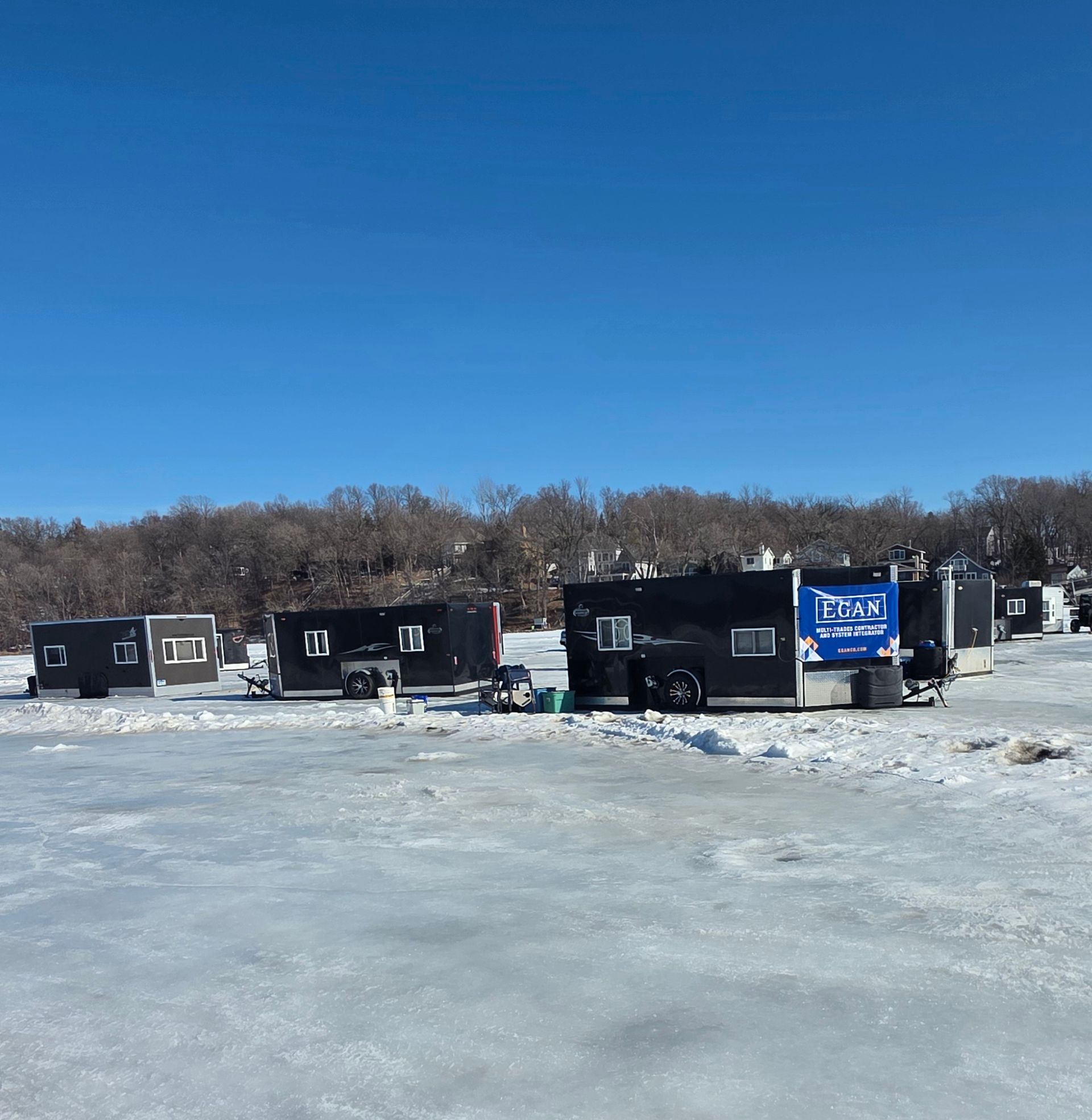 Black ice fishing shanties on a frozen lake under a clear blue sky