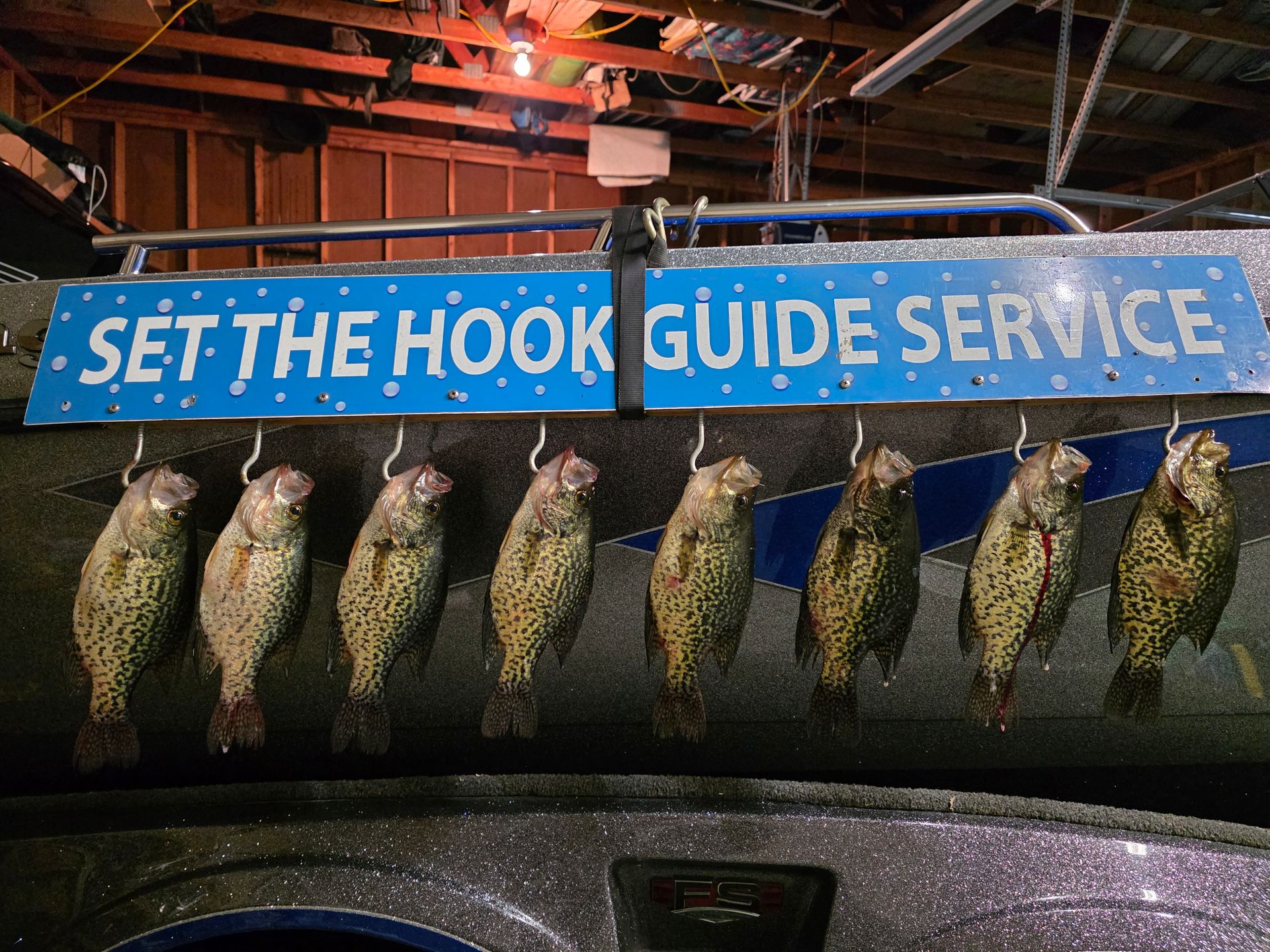 Blue sign reading “SET THE HOOK GUIDE SERVICE” above a row of hanging fish.