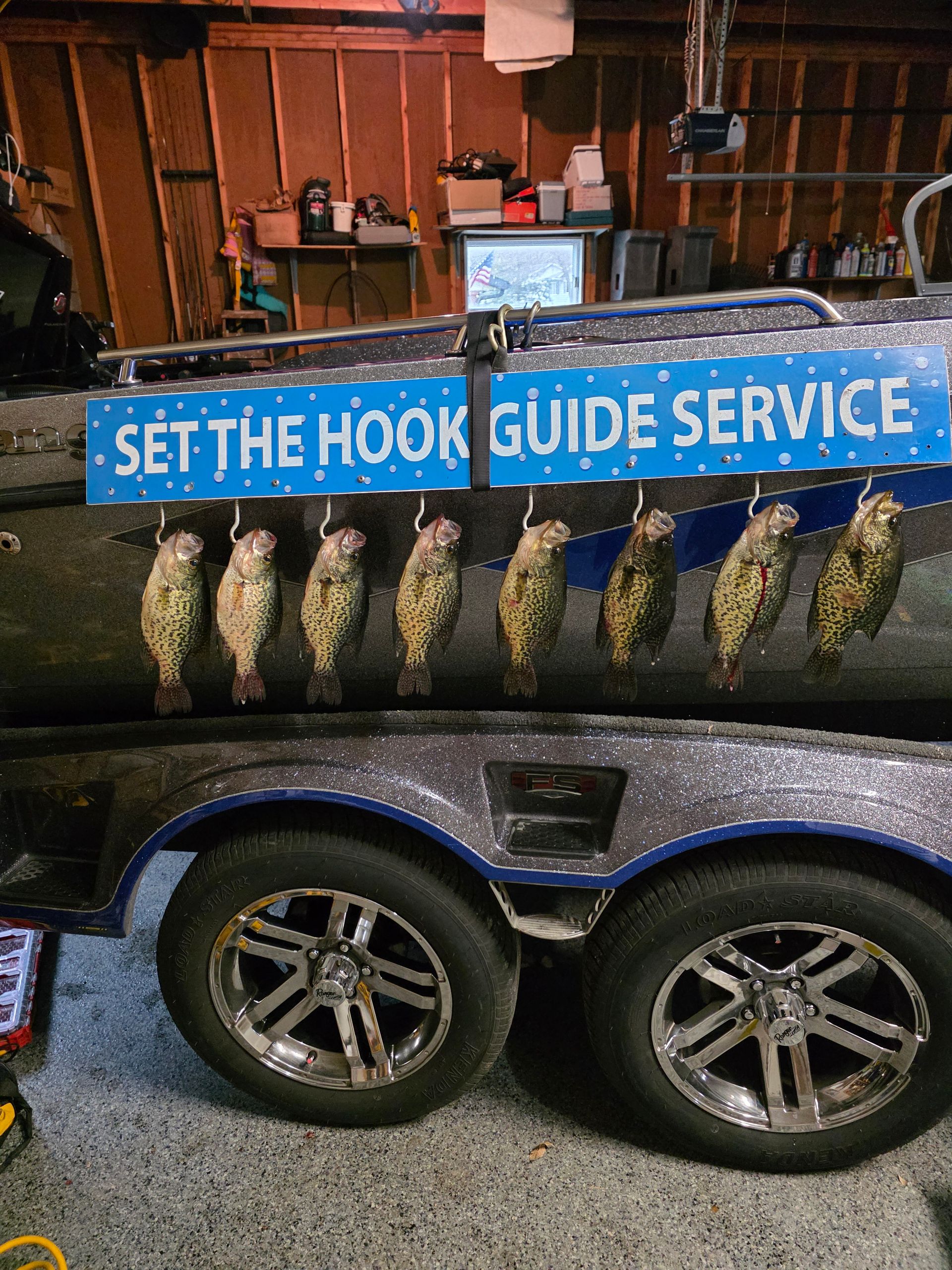 Blue bait signs reading “SET THE HOOK” and “GUIDE SERVICE” on a fishing trailer with hanging fish.