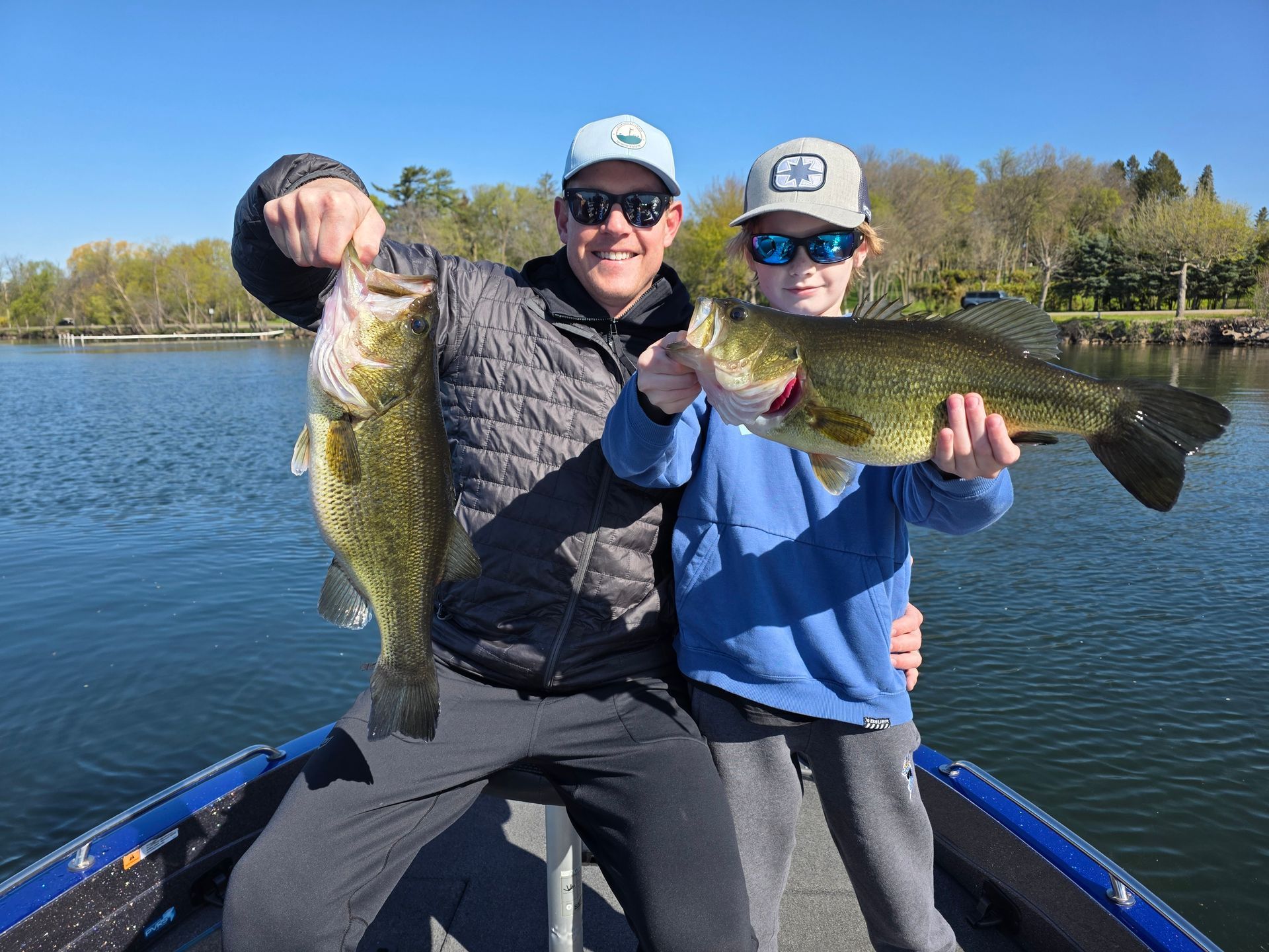 Three anglers on a boat holding large fish on a sunny lake
