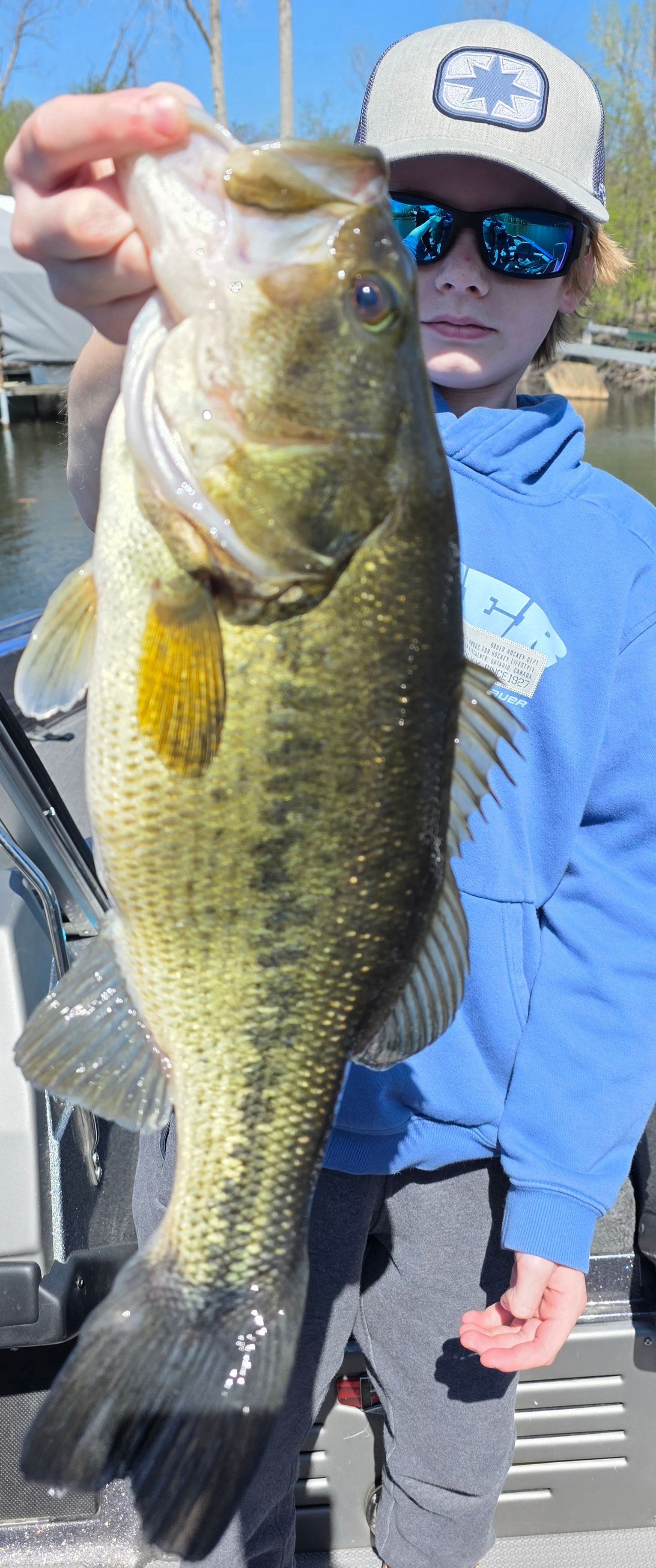 Angler in blue shirt and sunglasses holding a large bass by a boat railing