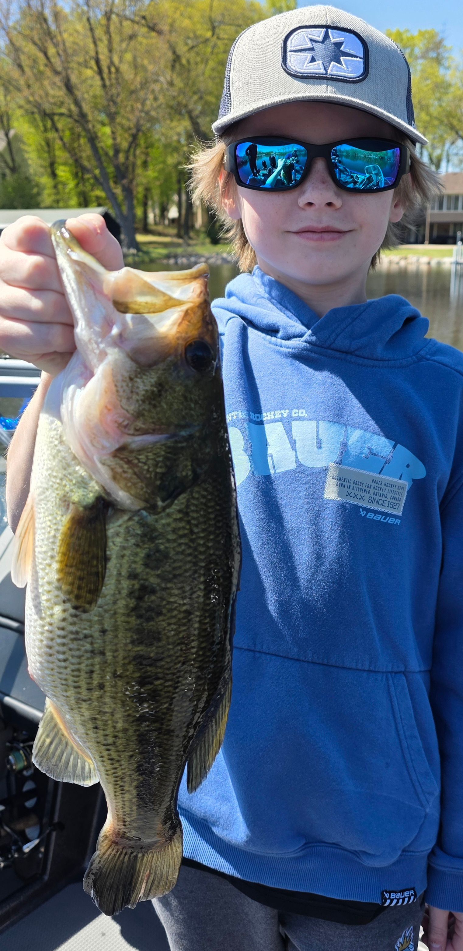 Youth in cap and sunglasses holding a large fish outdoors by the water