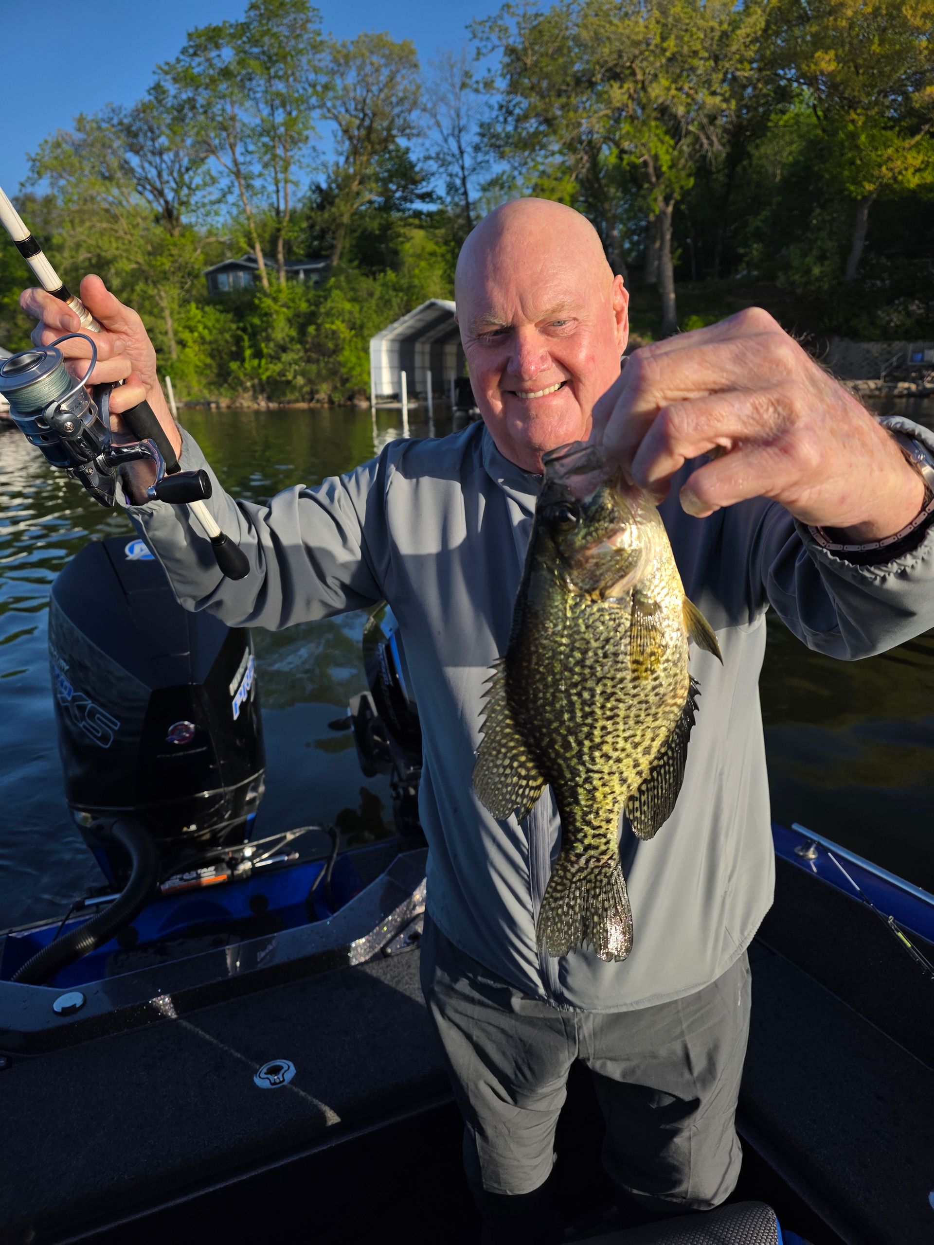 Man holding a fishing rod and a crappie on a boat at sunset.