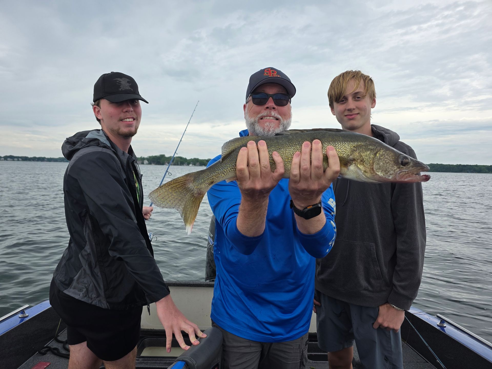 Three people on a boat hold up a large fish on a cloudy lake.