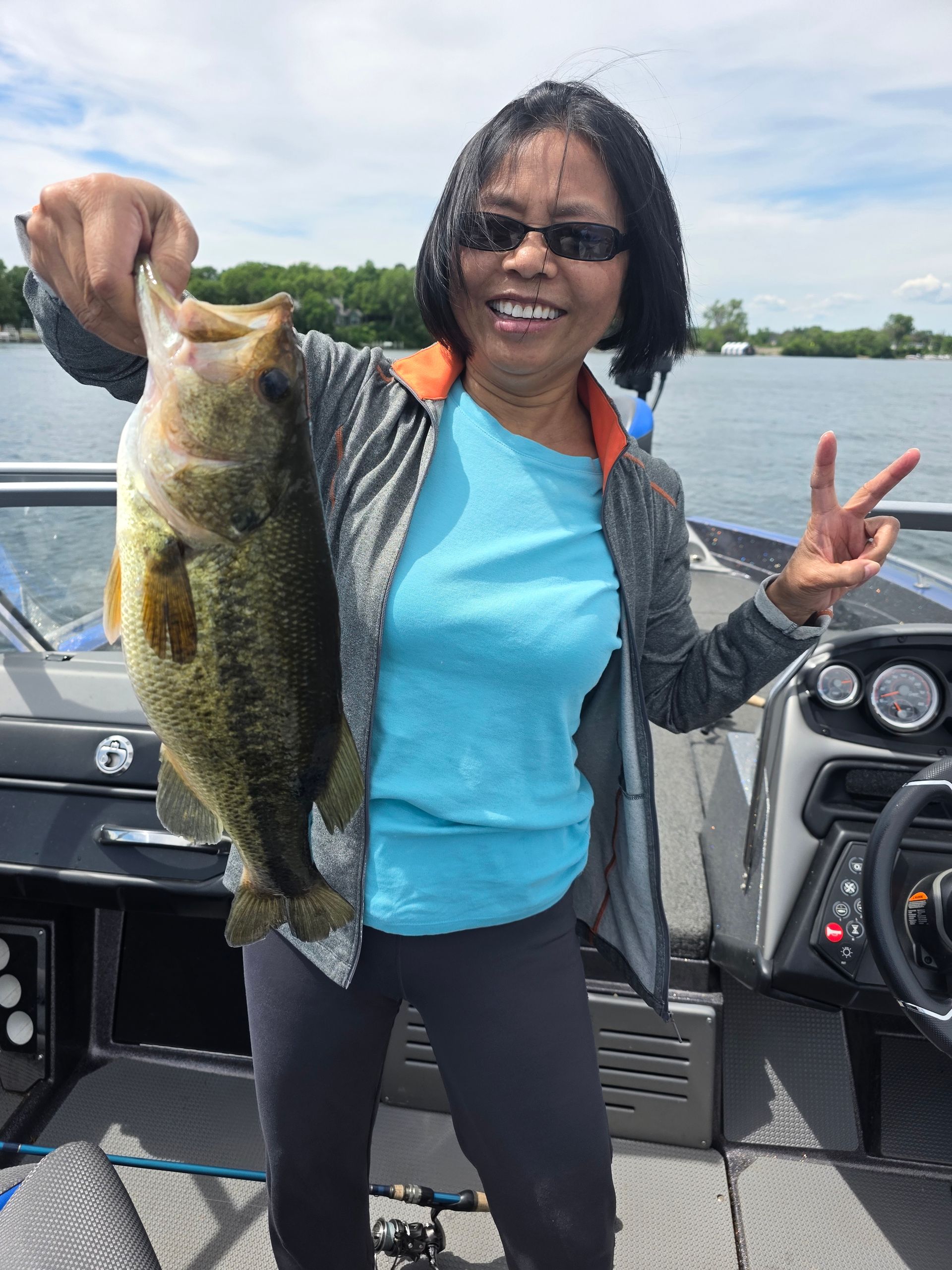 Person on a boat holding a large fish and making a peace sign, with water and trees in the background.
