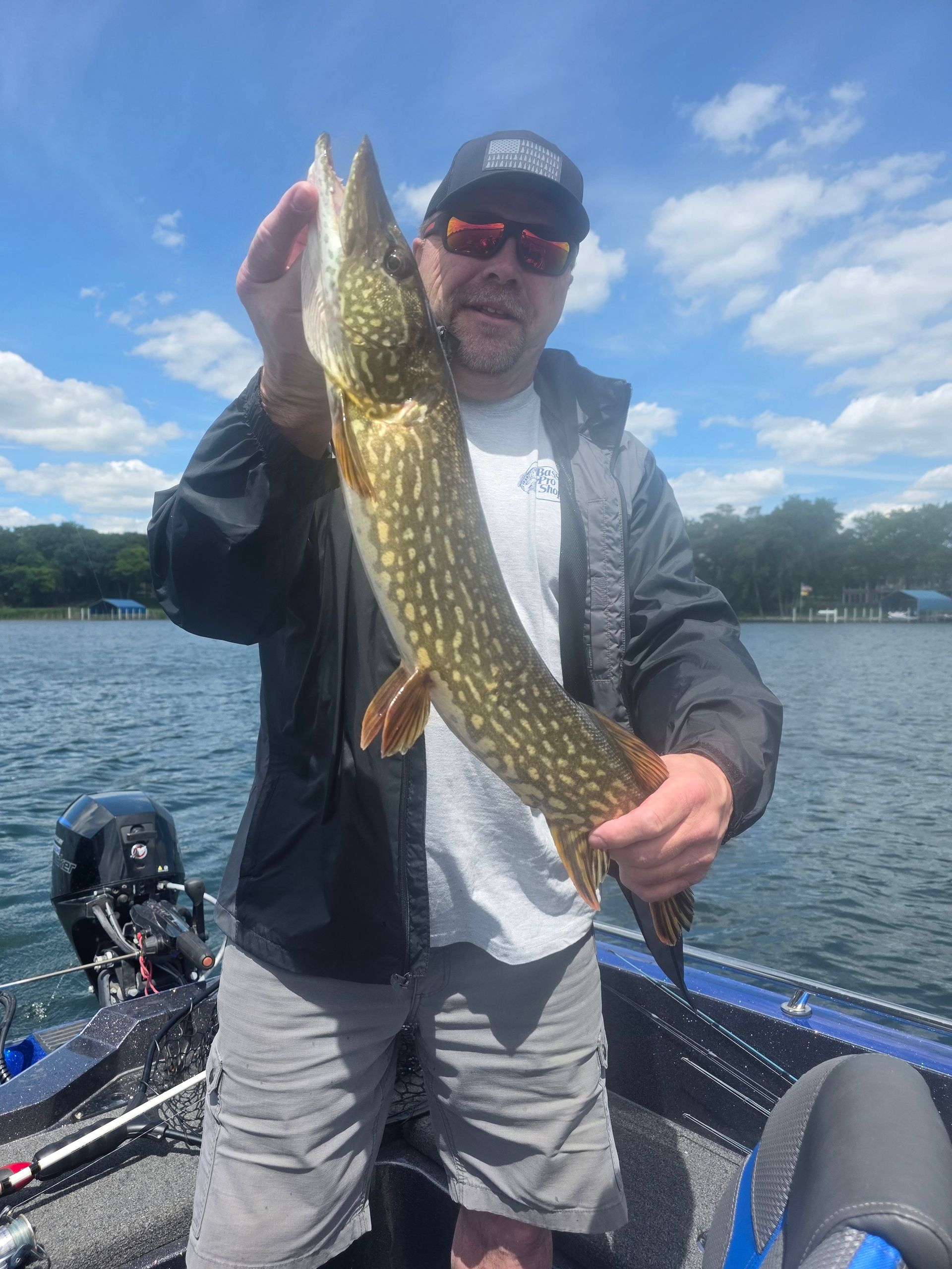 Person on a boat holding a large fish over the water under a blue sky.