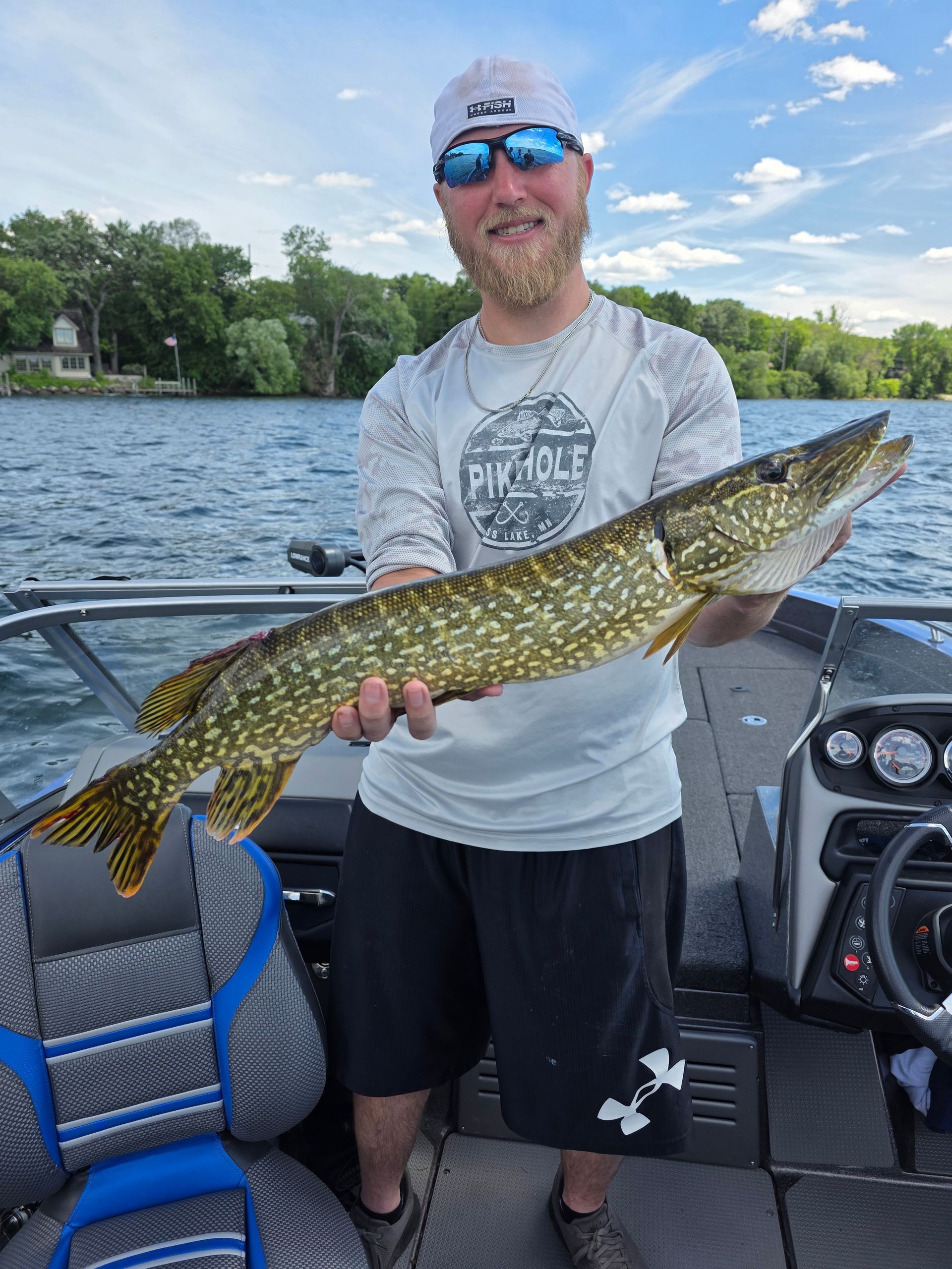 Person on a boat holding a large green-and-yellow fish on a lake under a cloudy sky