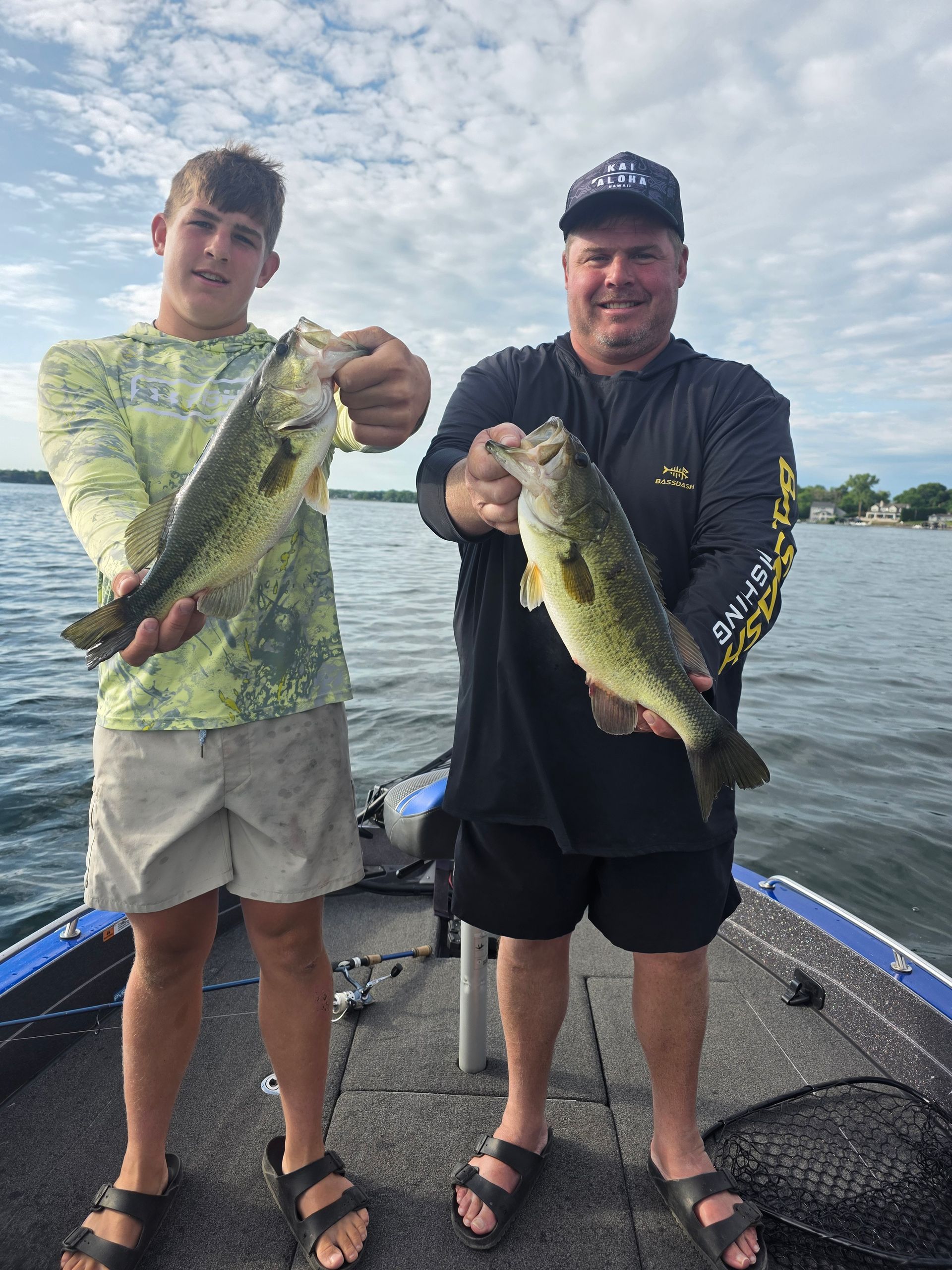 Two people on a boat hold up largemouth bass against a cloudy sky.
