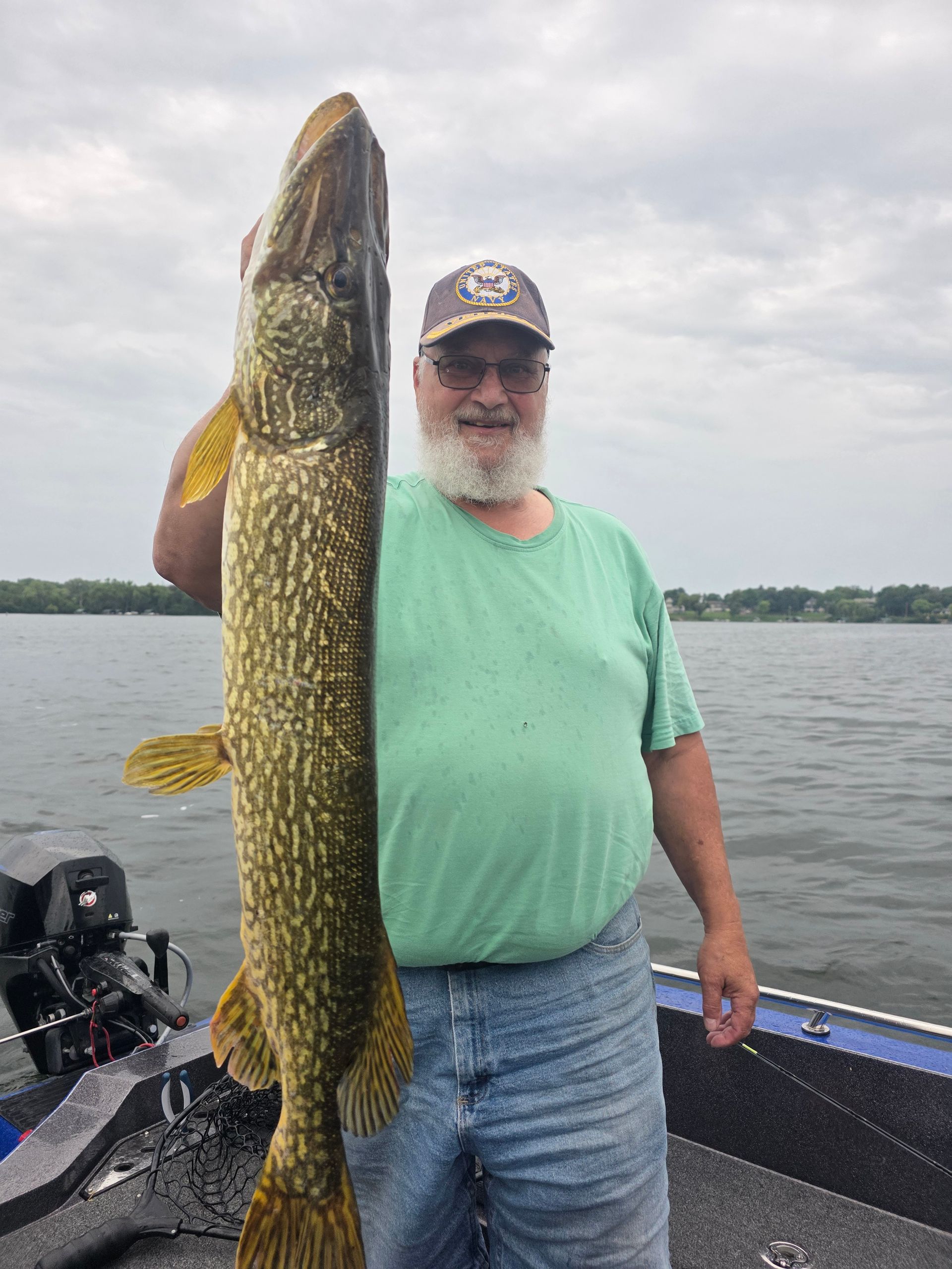 Man holding a large northern pike on a boat on a lake under cloudy skies