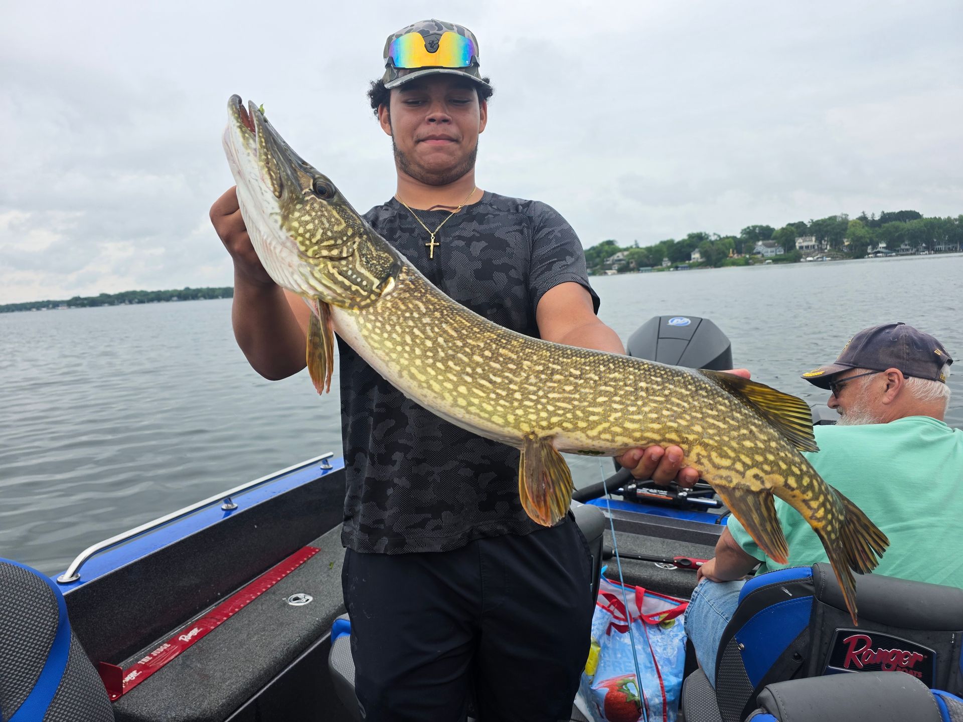Angler on a boat holds a large spotted fish on a lake.