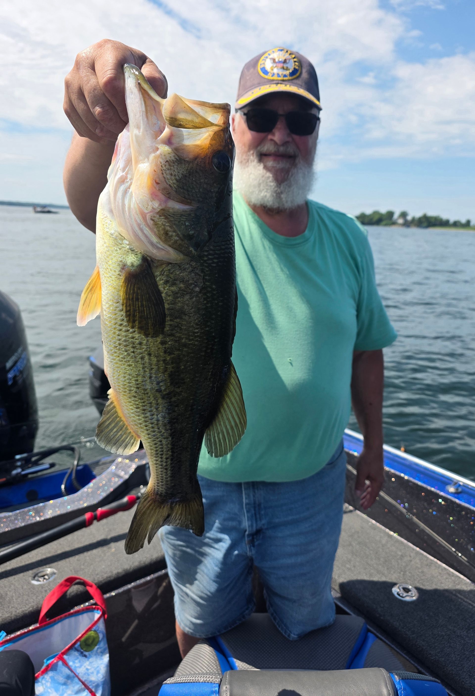 Man holding a large bass on a boat on a lake under a partly cloudy sky