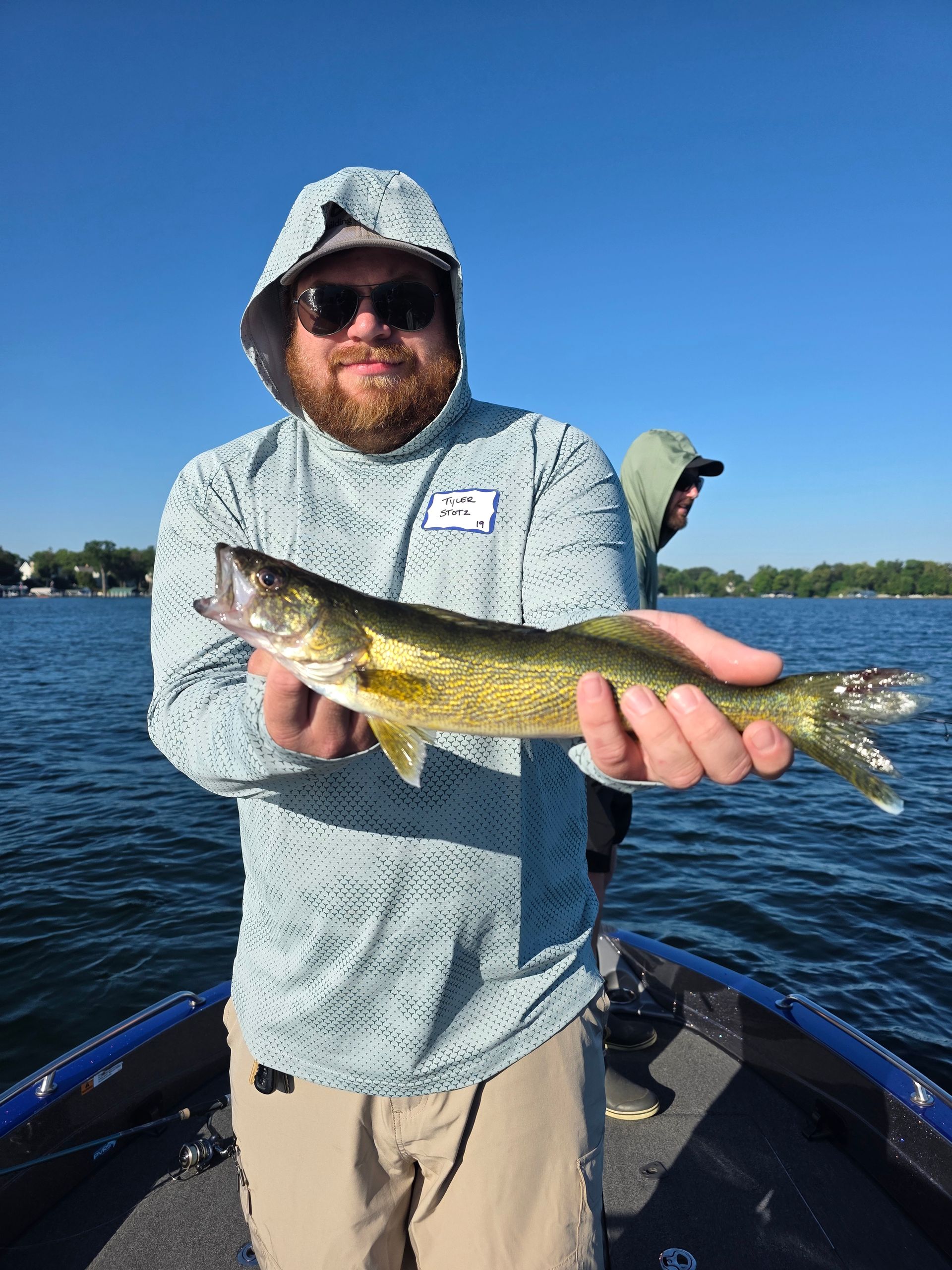 Person on a boat holding a fish over the water on a sunny day