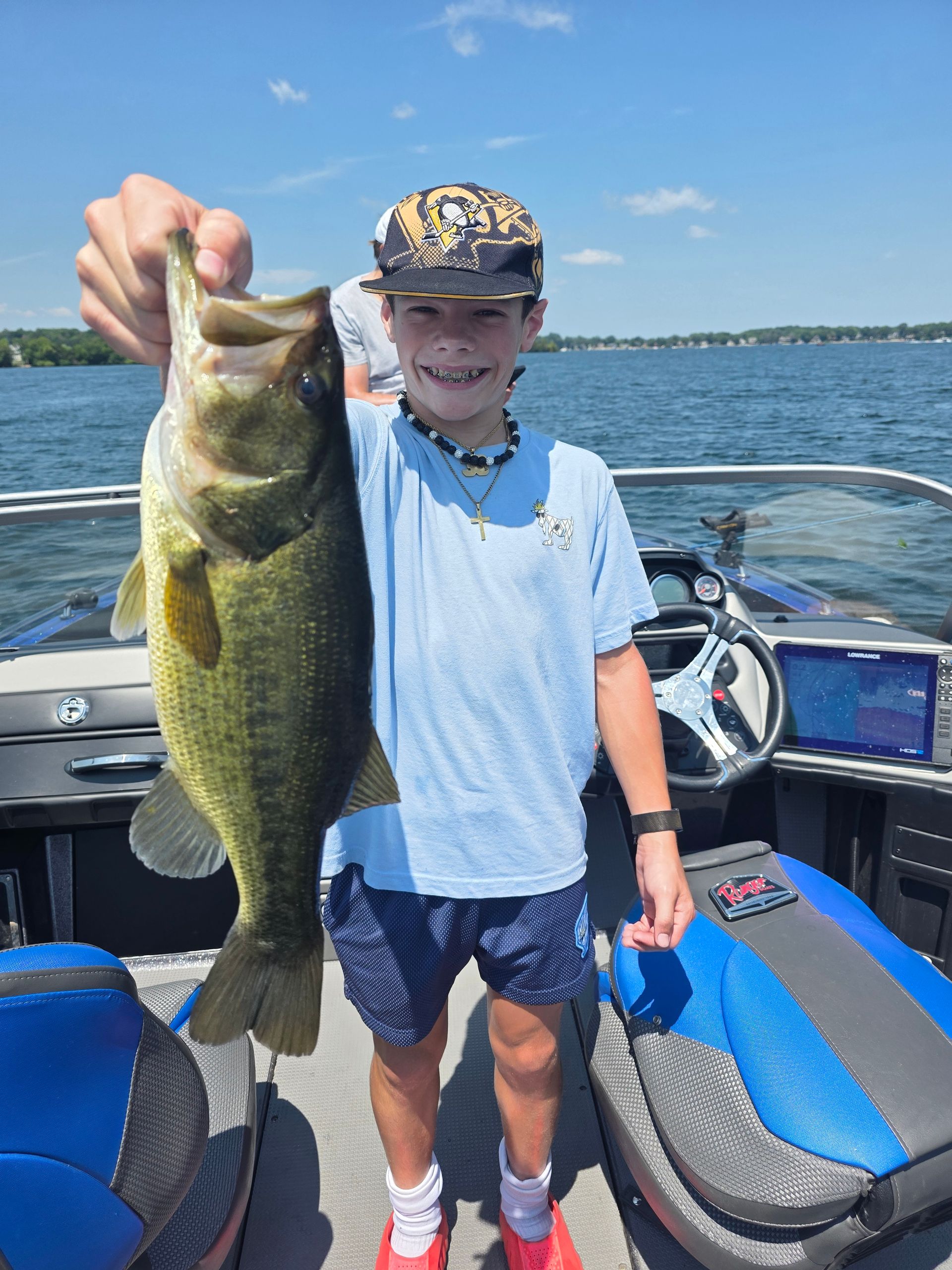 Smiling angler on a boat holding a large bass on a sunny lake