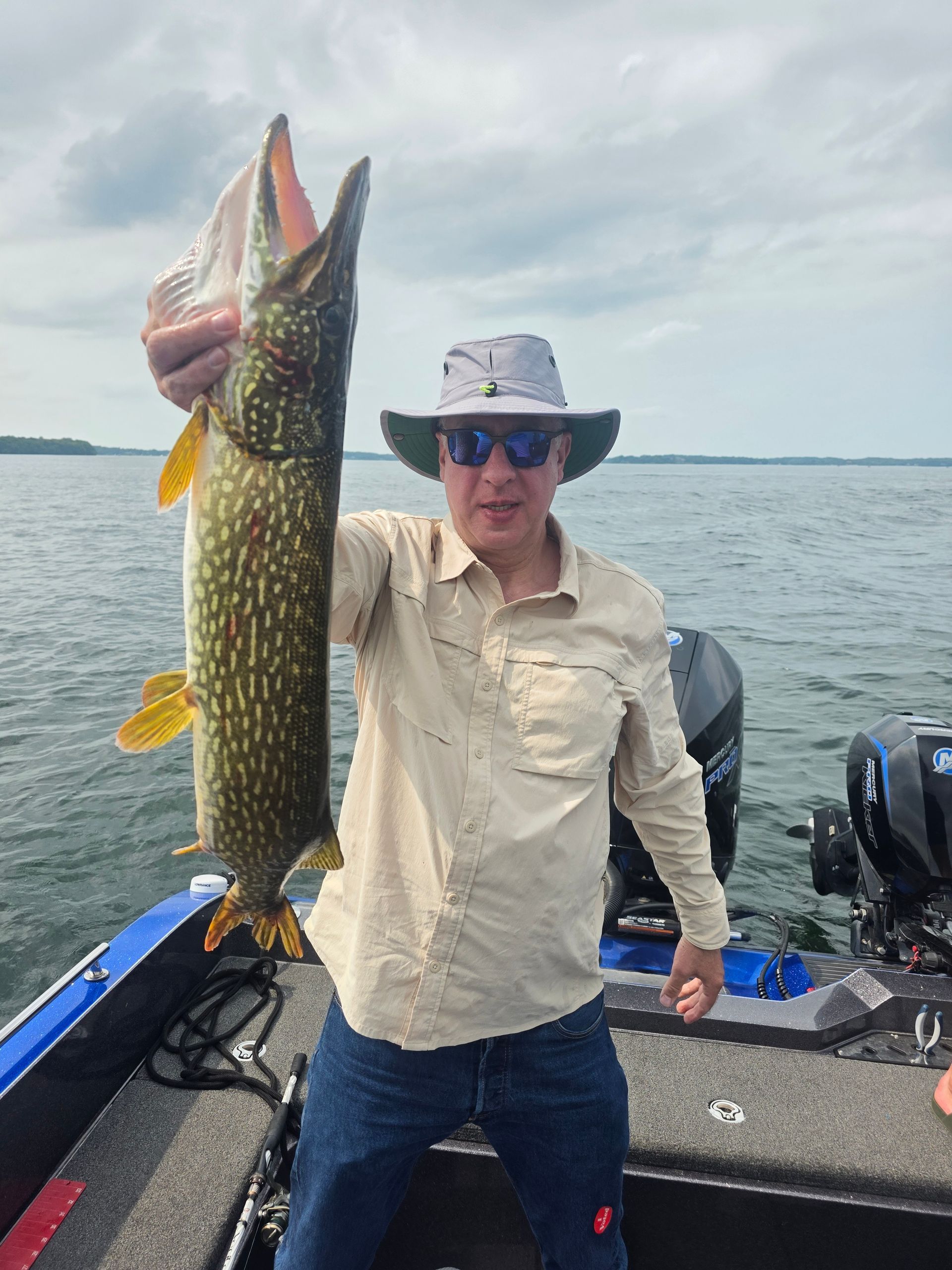 Angler on a boat holding a large northern pike over the water.