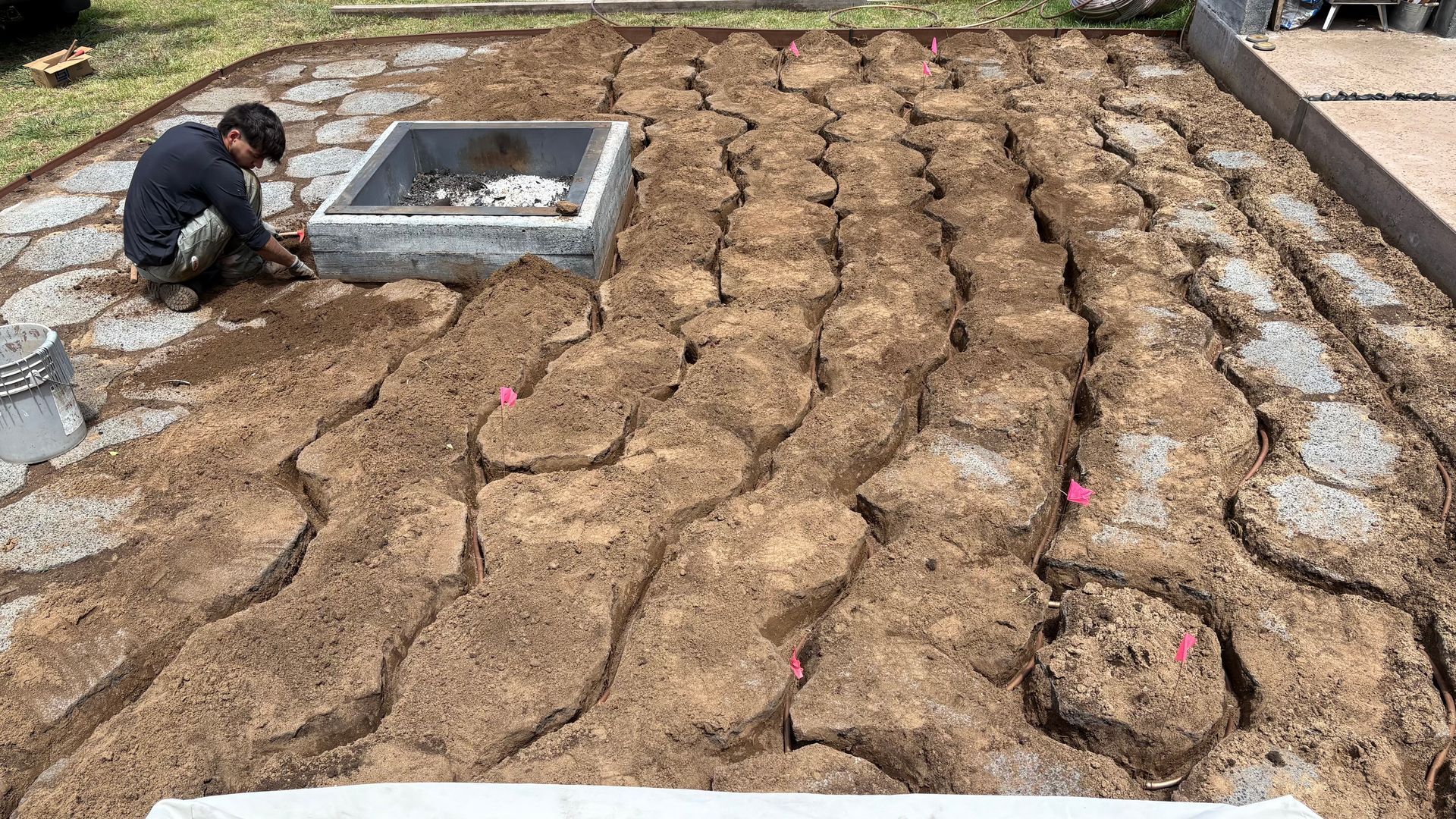 Man working in garden, filling spaces between stone pavers with soil. Outdoor setting.