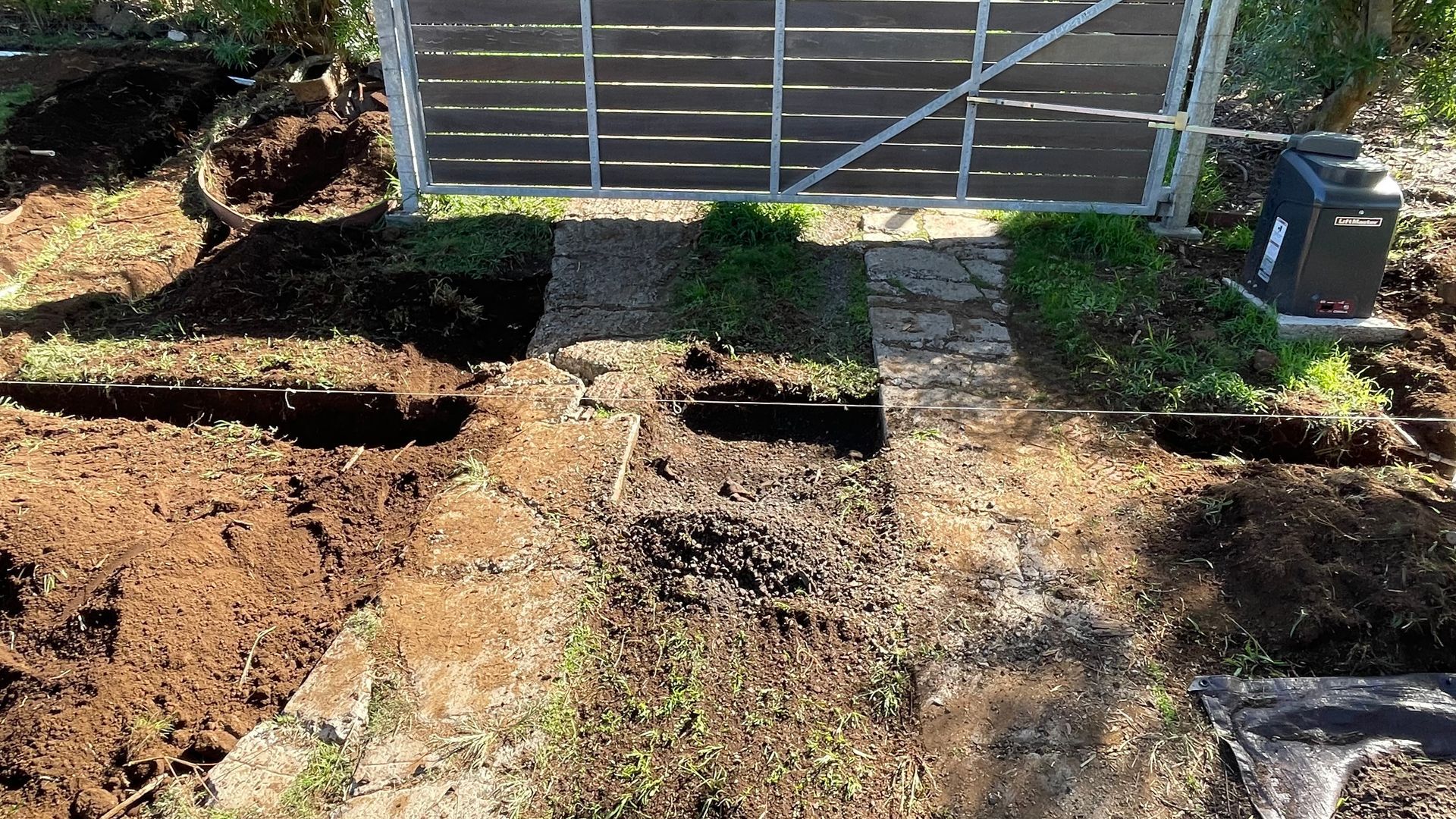 Dirt-covered yard with partially built path to a gate; grass and earth are scattered about.