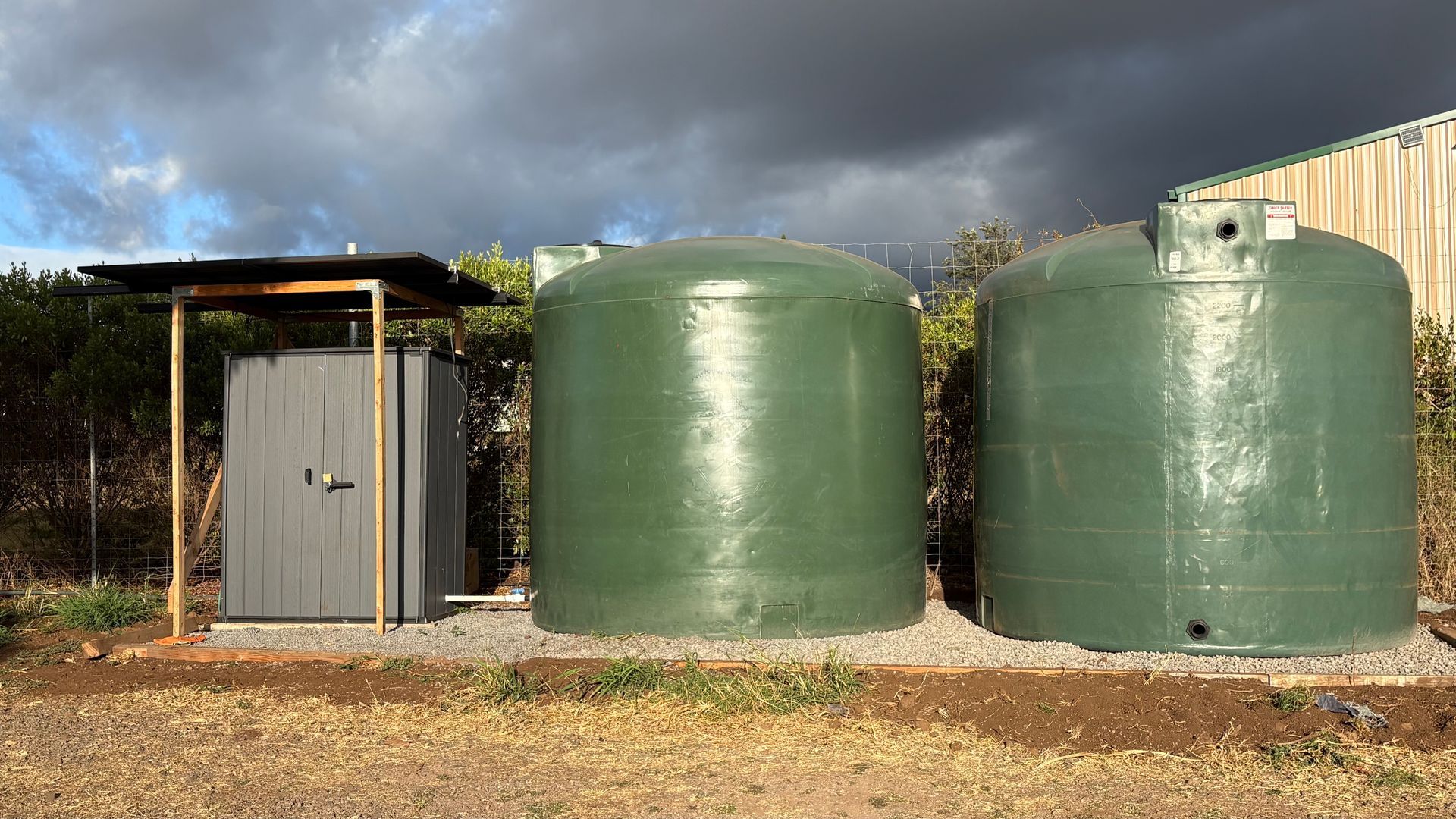 Two green water tanks and a gray shed under a cloudy sky.