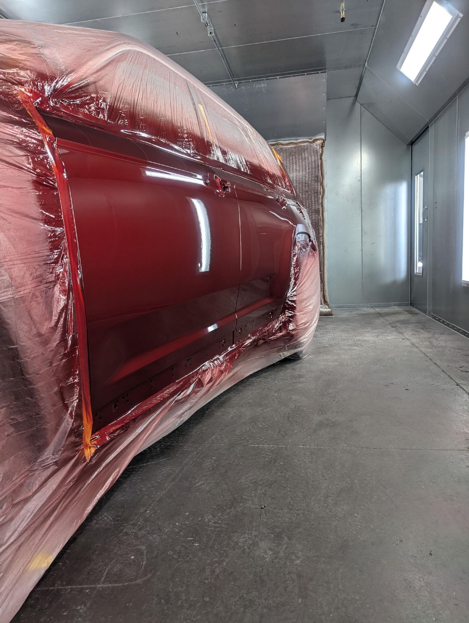 Red car part in an auto paint booth, metallic color, curved shape, reflection on shiny surface.