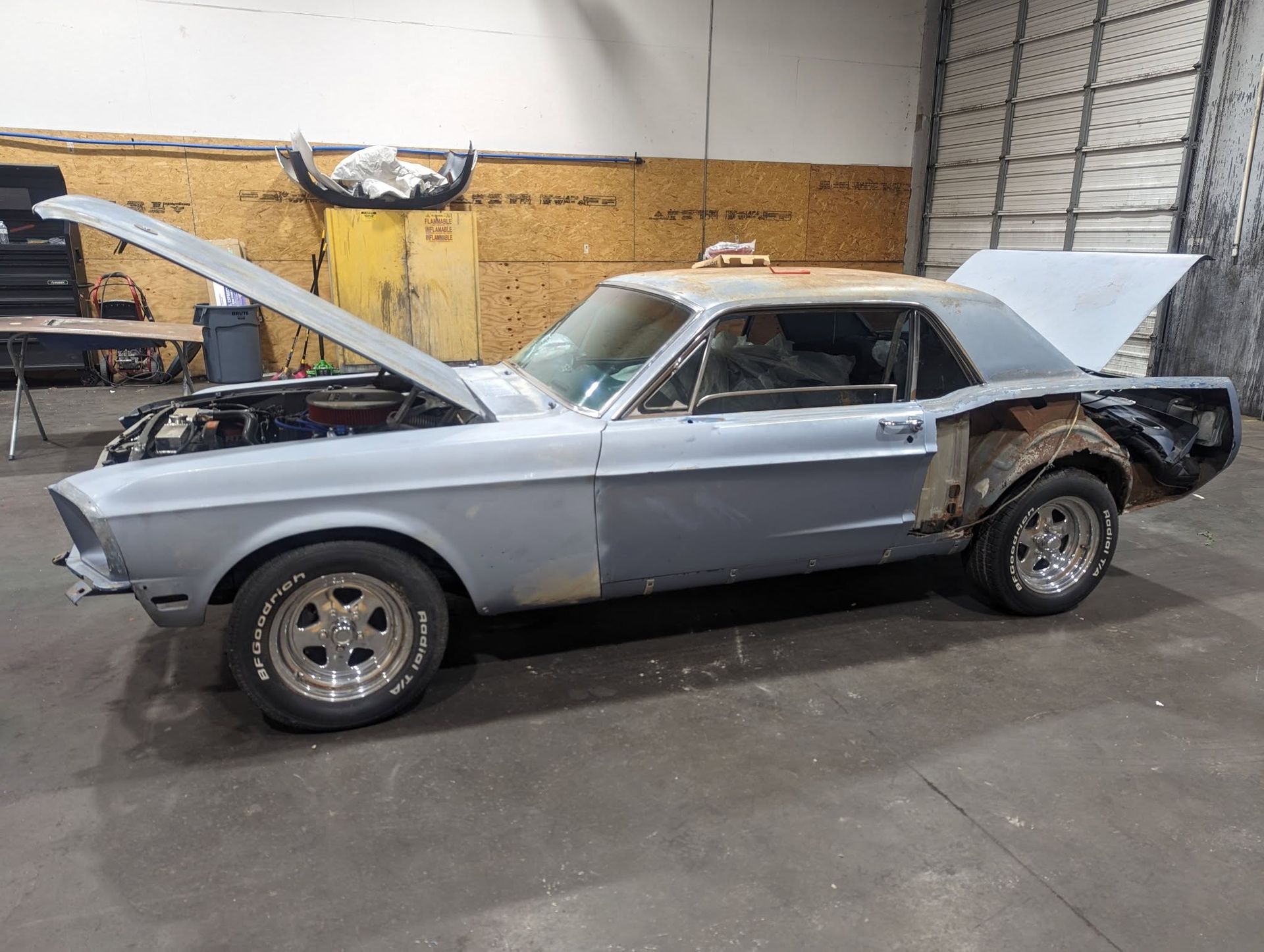 Gray classic Mustang car in a shop with hood and trunk open, undergoing restoration.