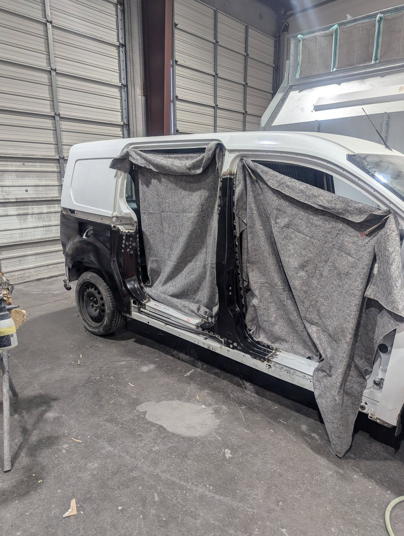 White van in a shop, partially disassembled, covered with gray fabric.