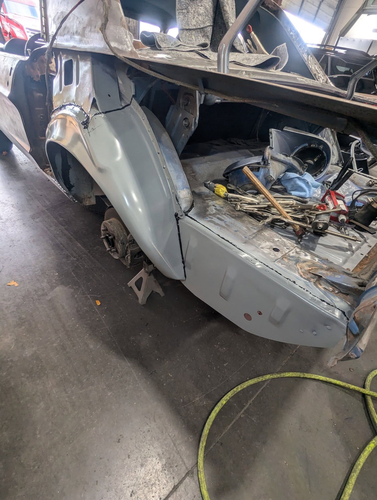 Car undergoing restoration with a grey fender installed. Workshop setting, car partially disassembled.