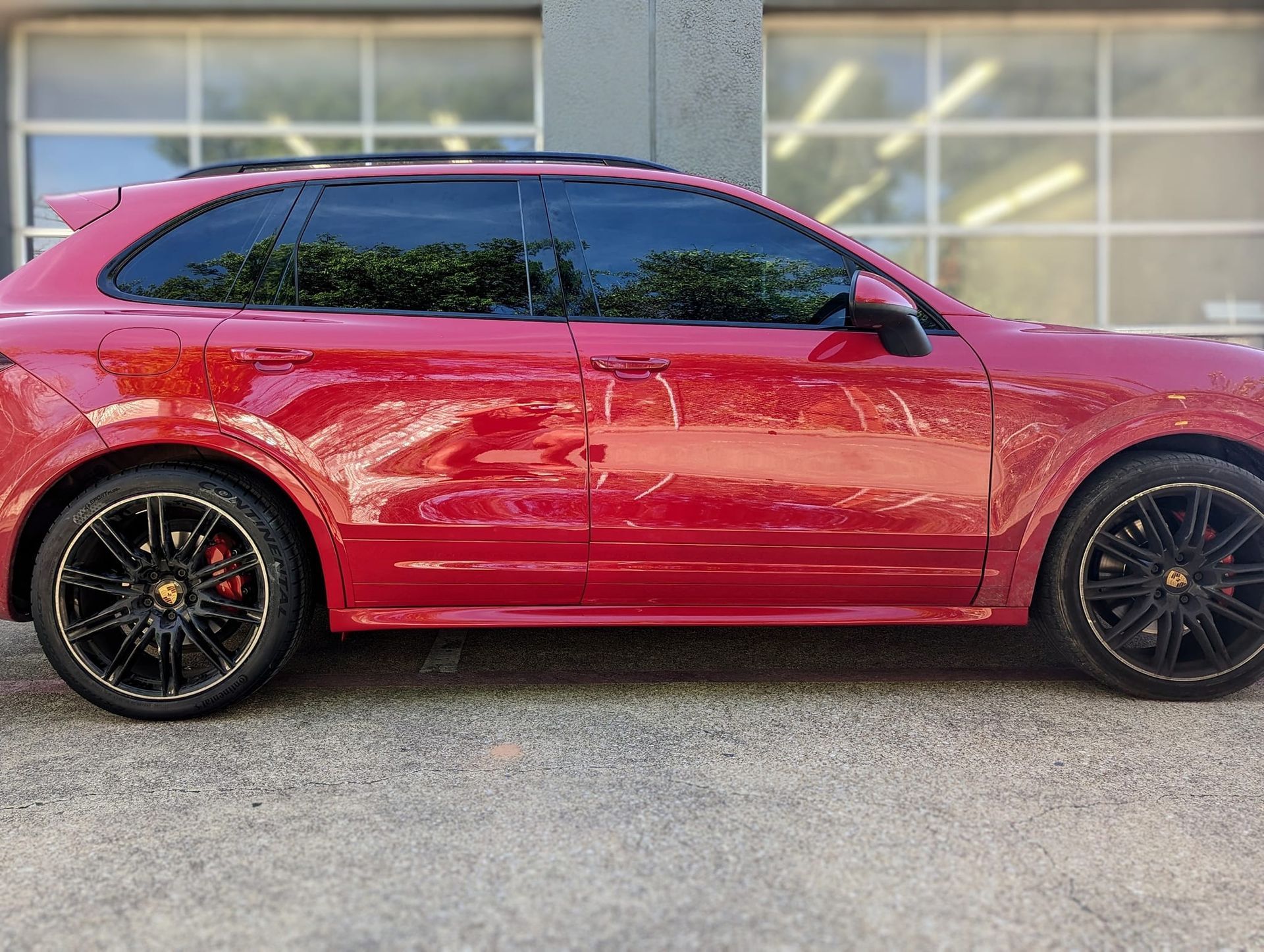 Red Porsche SUV with tinted windows and black rims parked outside.