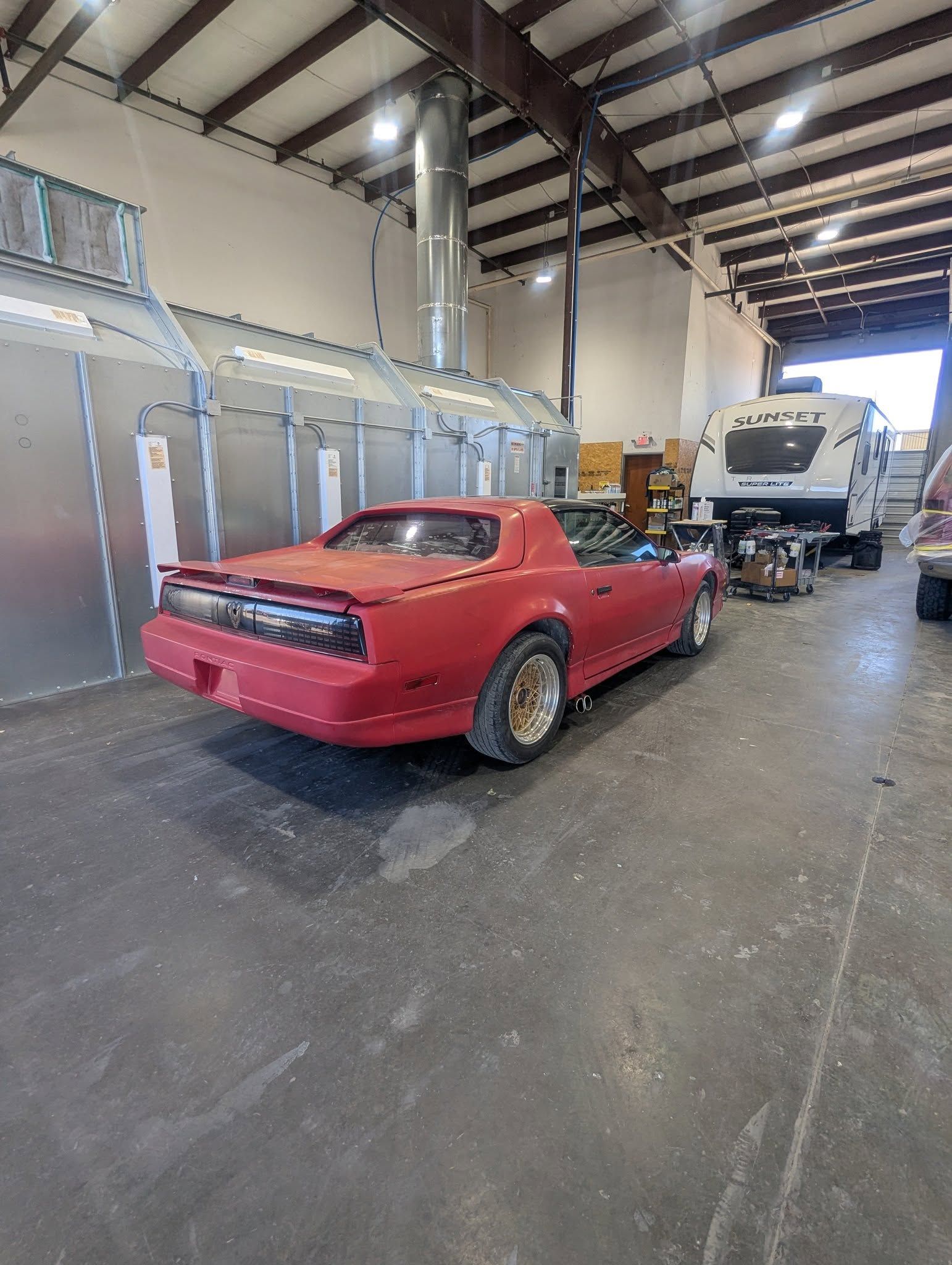 Red classic car inside a garage with a trailer in the background.