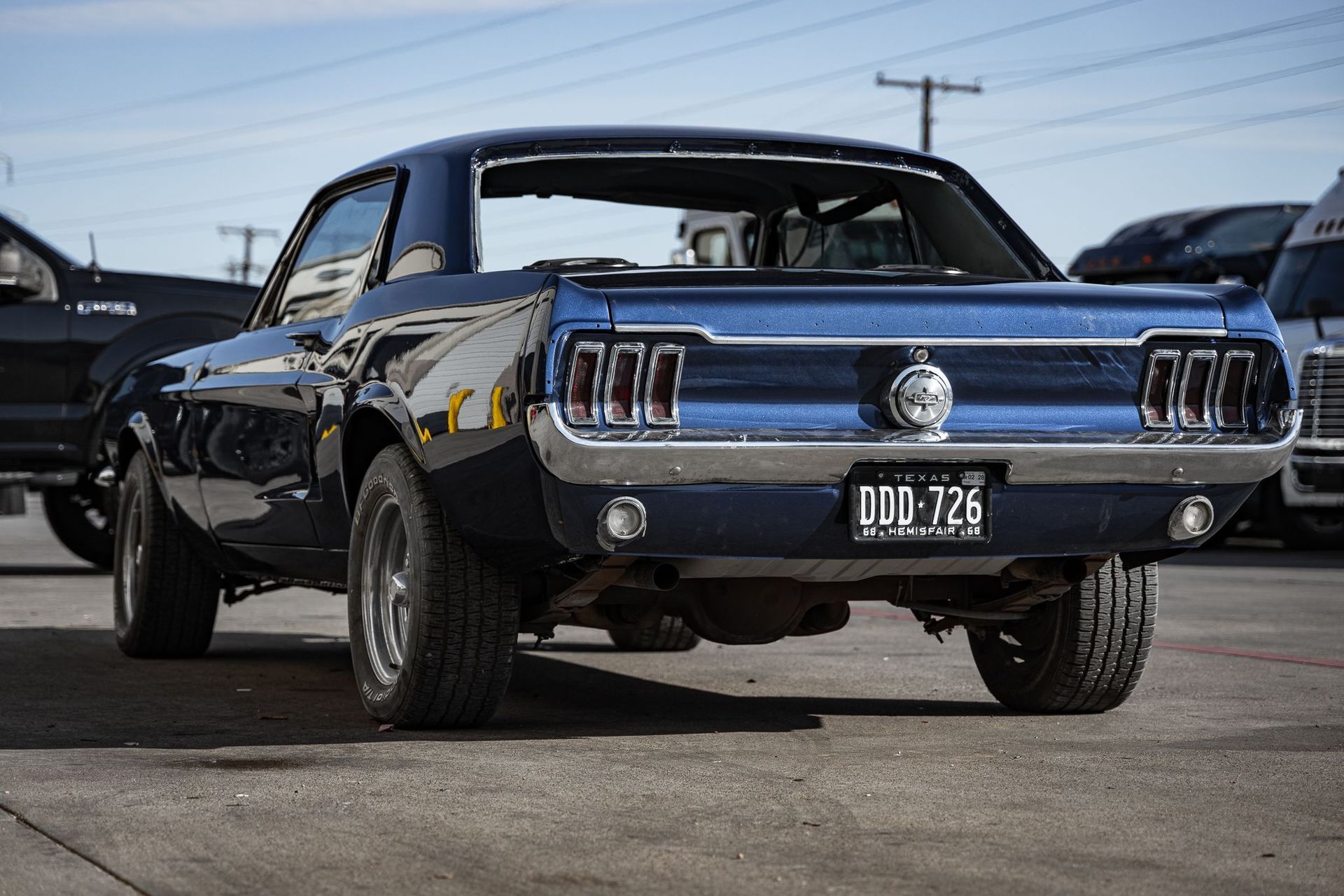 Dark blue vintage Ford Mustang with large tires, parked on pavement, rear view.