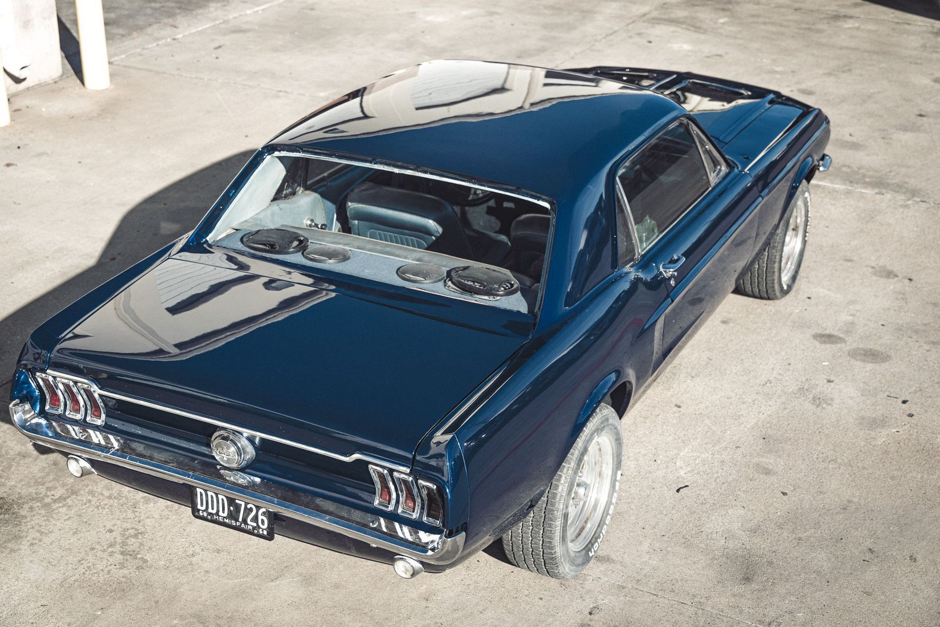 Blue vintage Ford Mustang coupe, parked outdoors. Shiny paint, large tires, sunny day.