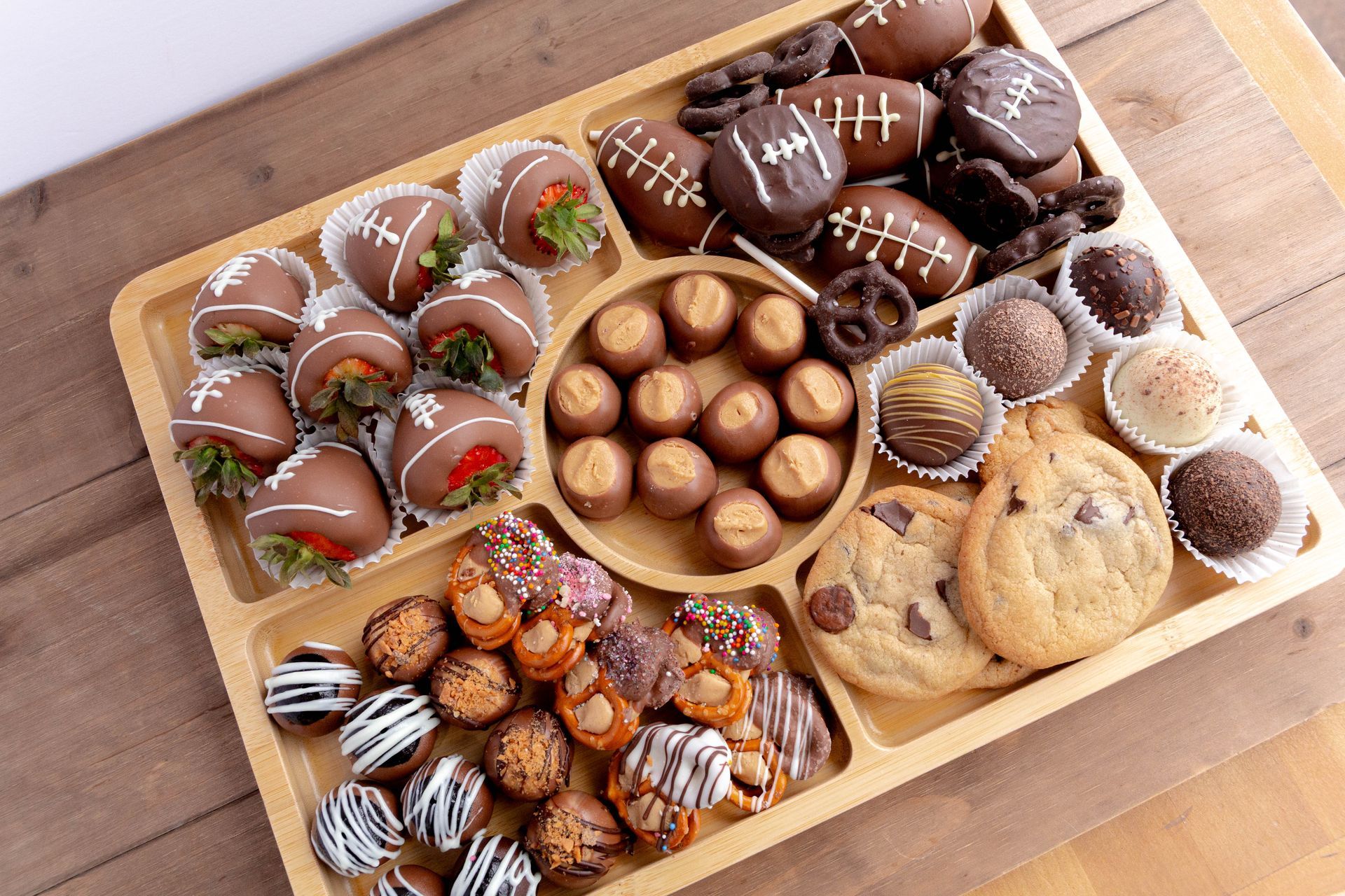 Dessert platter with chocolate-covered strawberries, football-shaped treats, truffles, cookies, and pretzels.