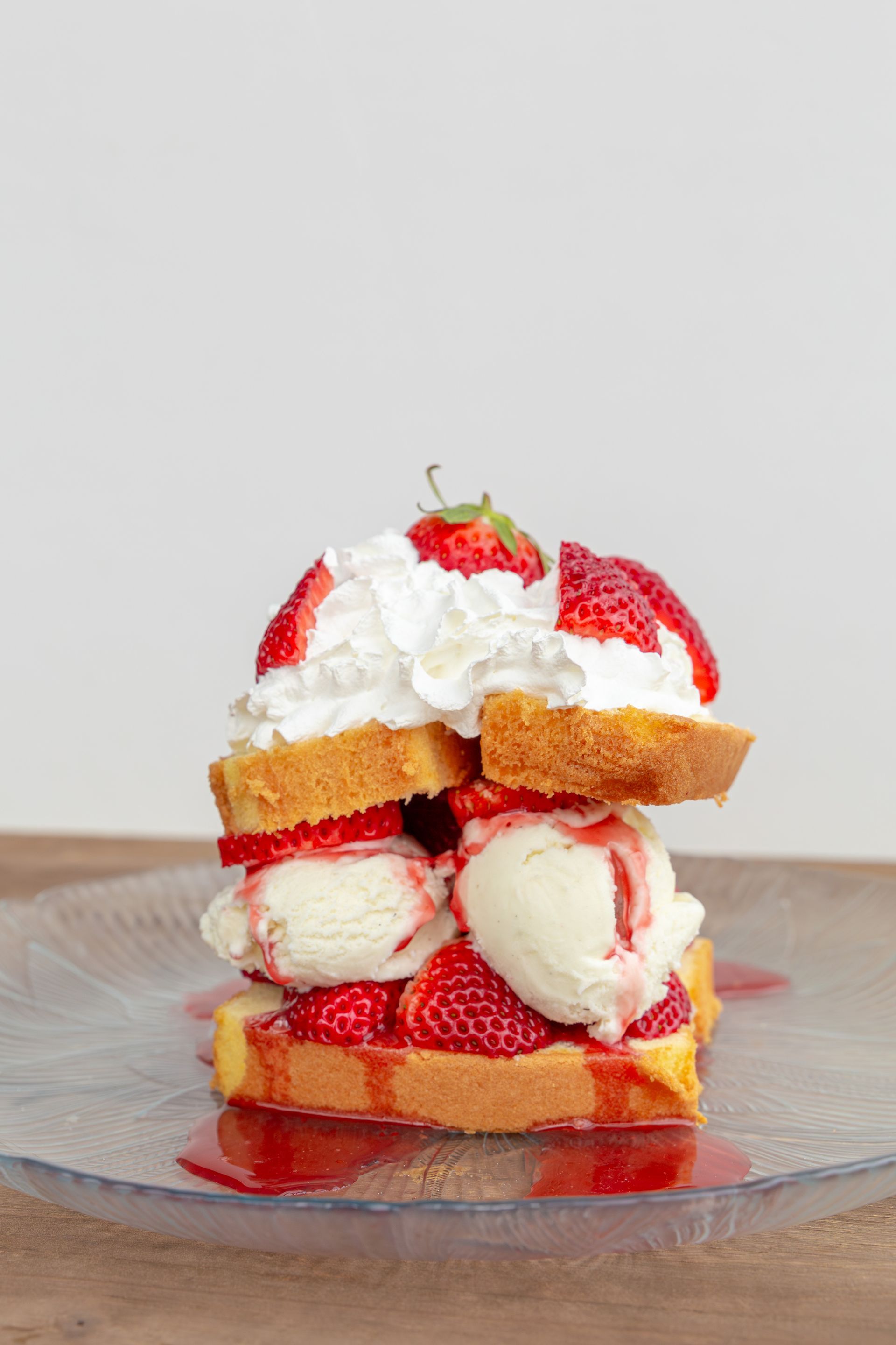 Strawberry shortcake with whipped cream and ice cream stacked on a clear plate.