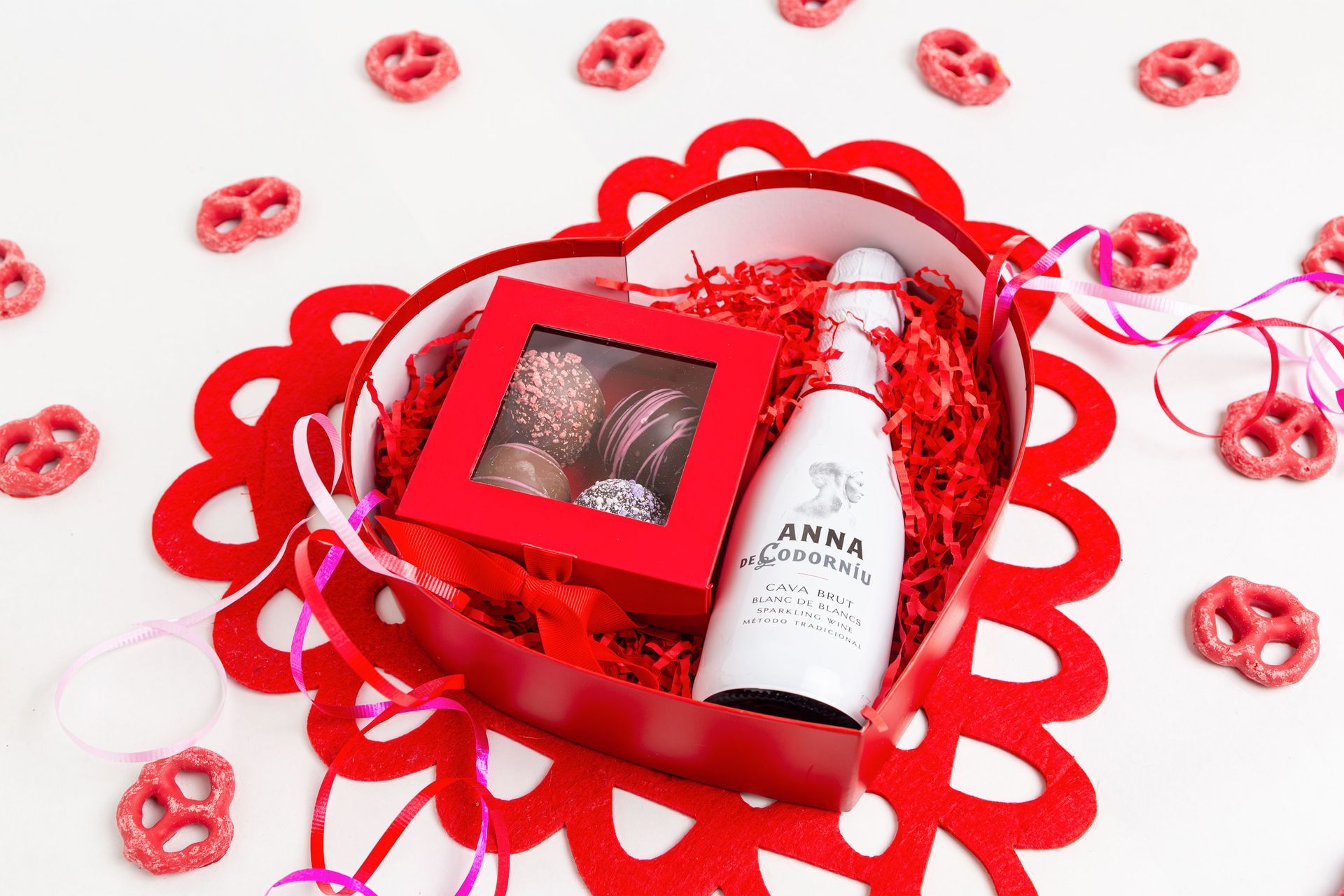 Valentine's Day gift: heart-shaped box with champagne, chocolates, and red-frosted pretzels.