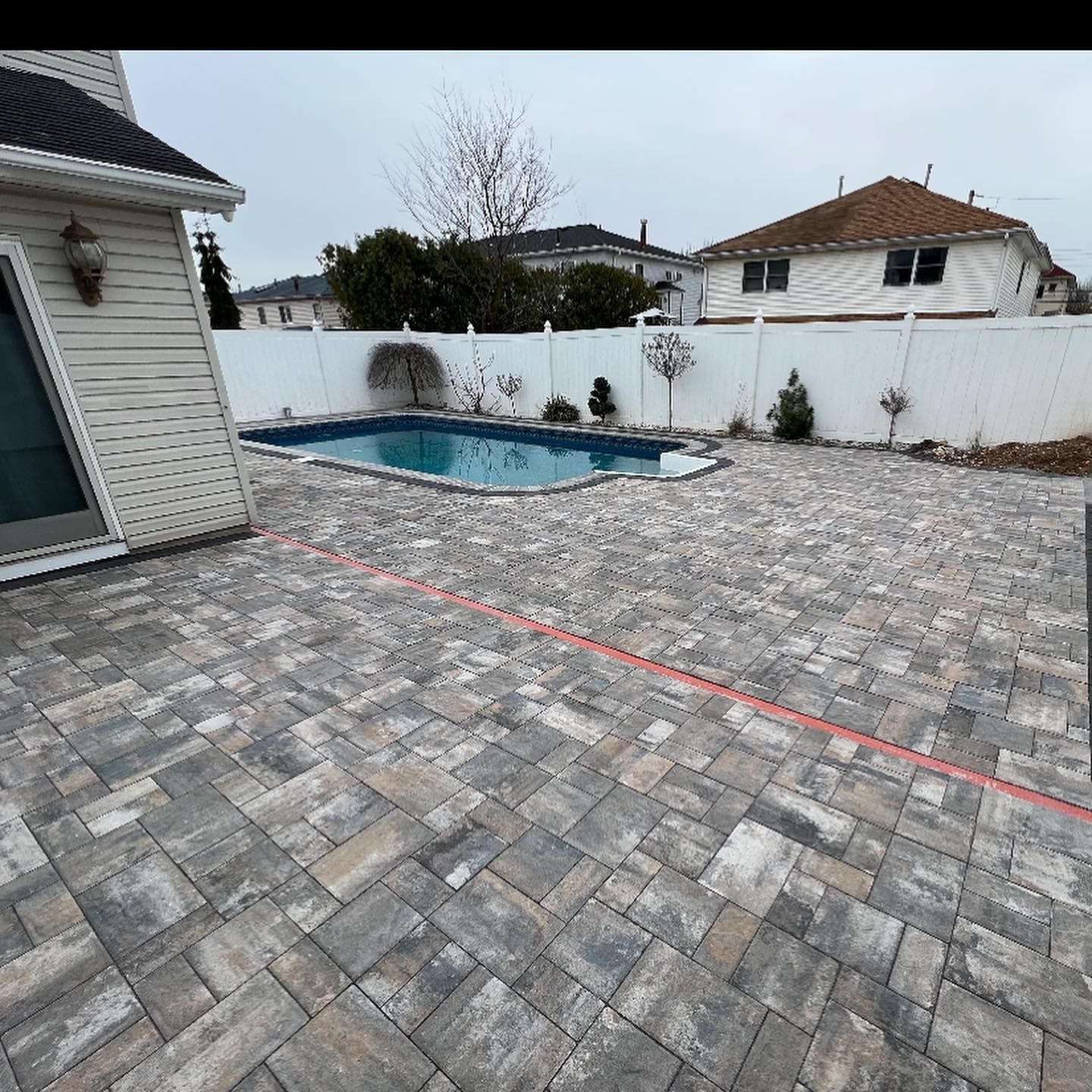 A brick patio with a pool in the backyard of a house.