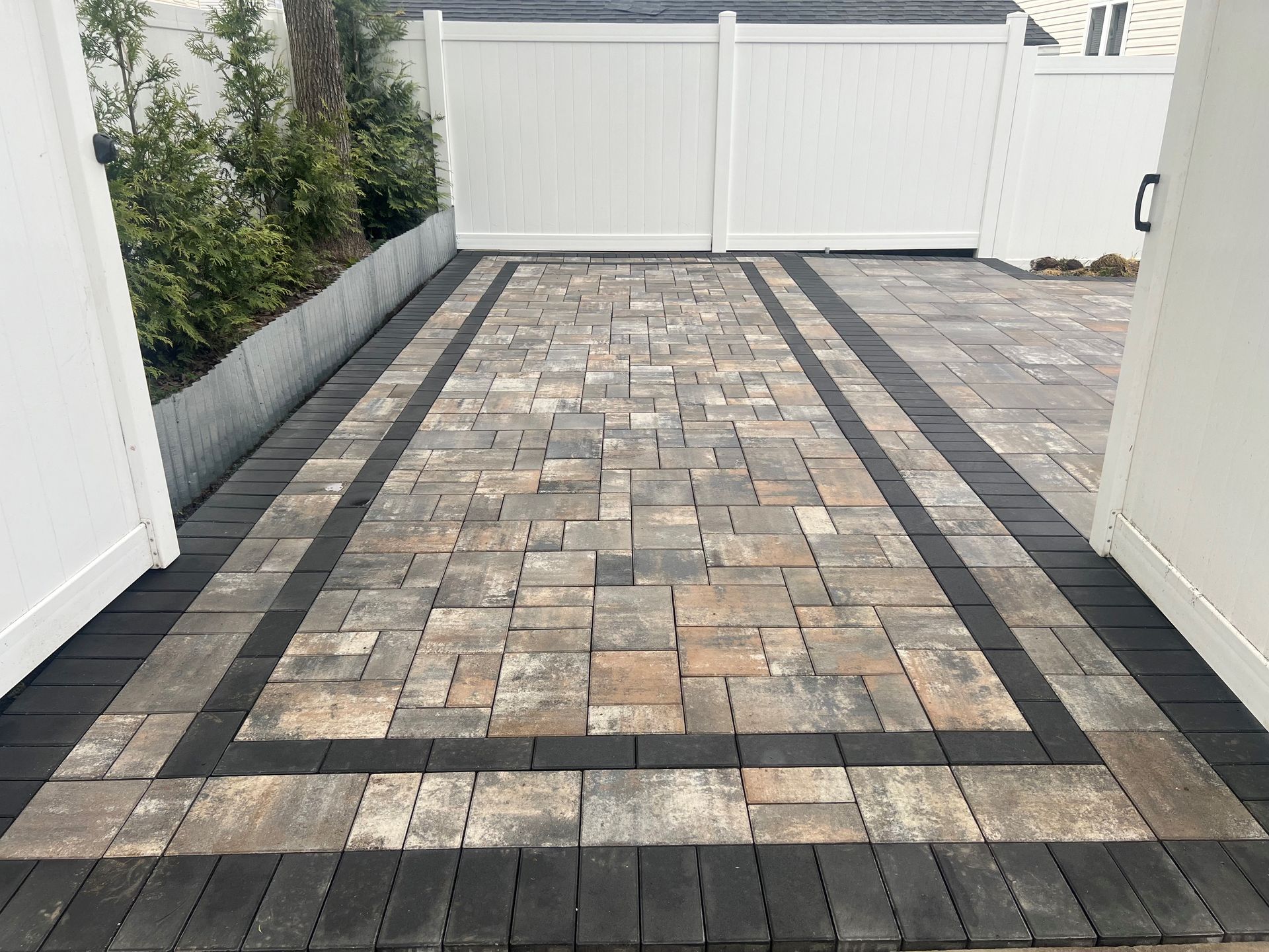 A brick driveway with a white fence in the background.