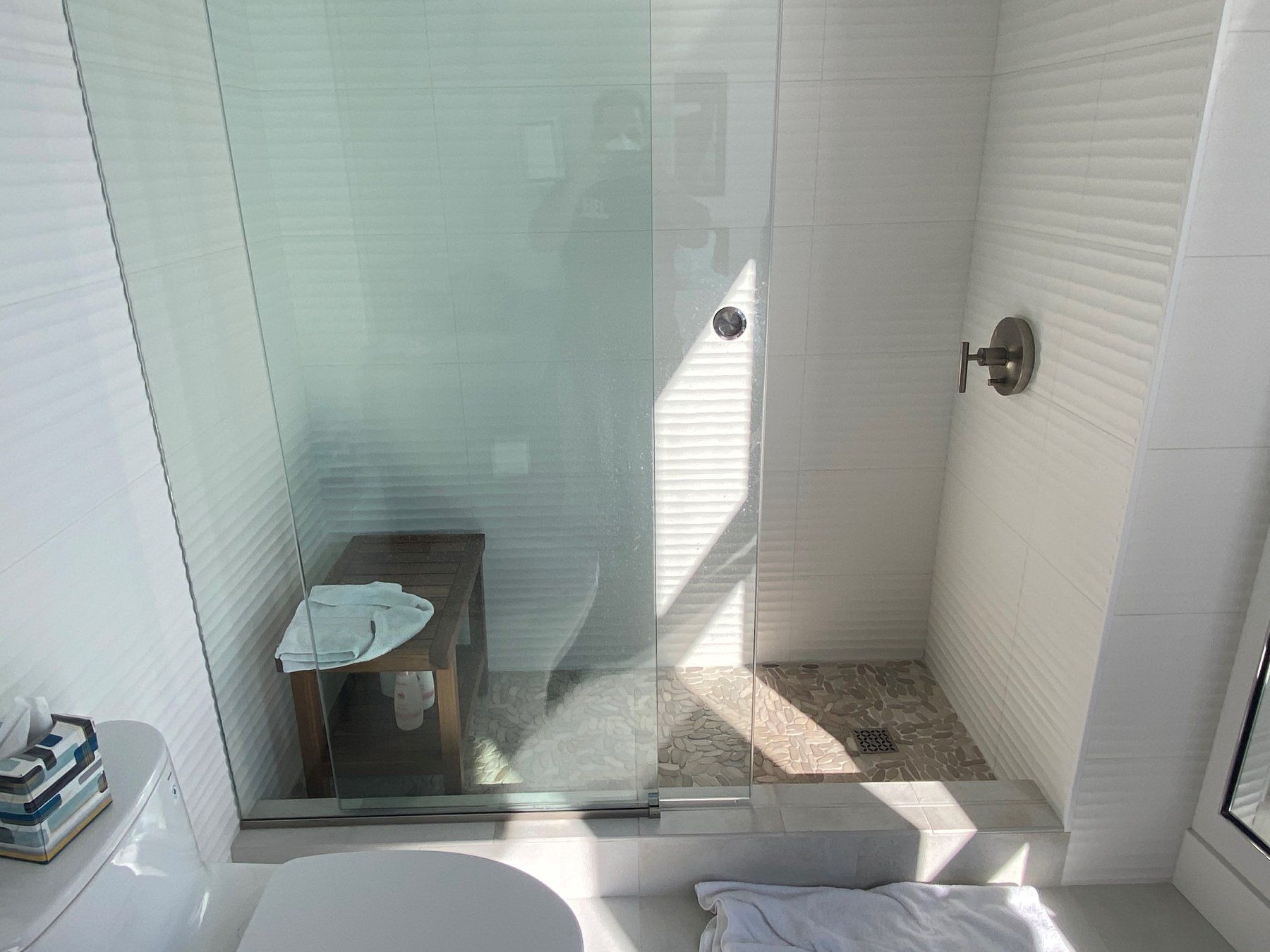 A bathroom with a toilet , shower , and bench.