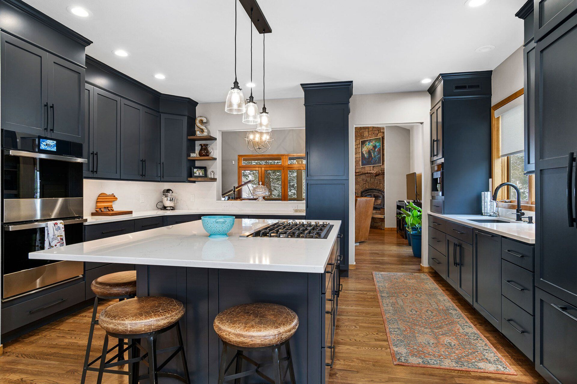 A kitchen with blue cabinets , white counter tops , stools and a large island.