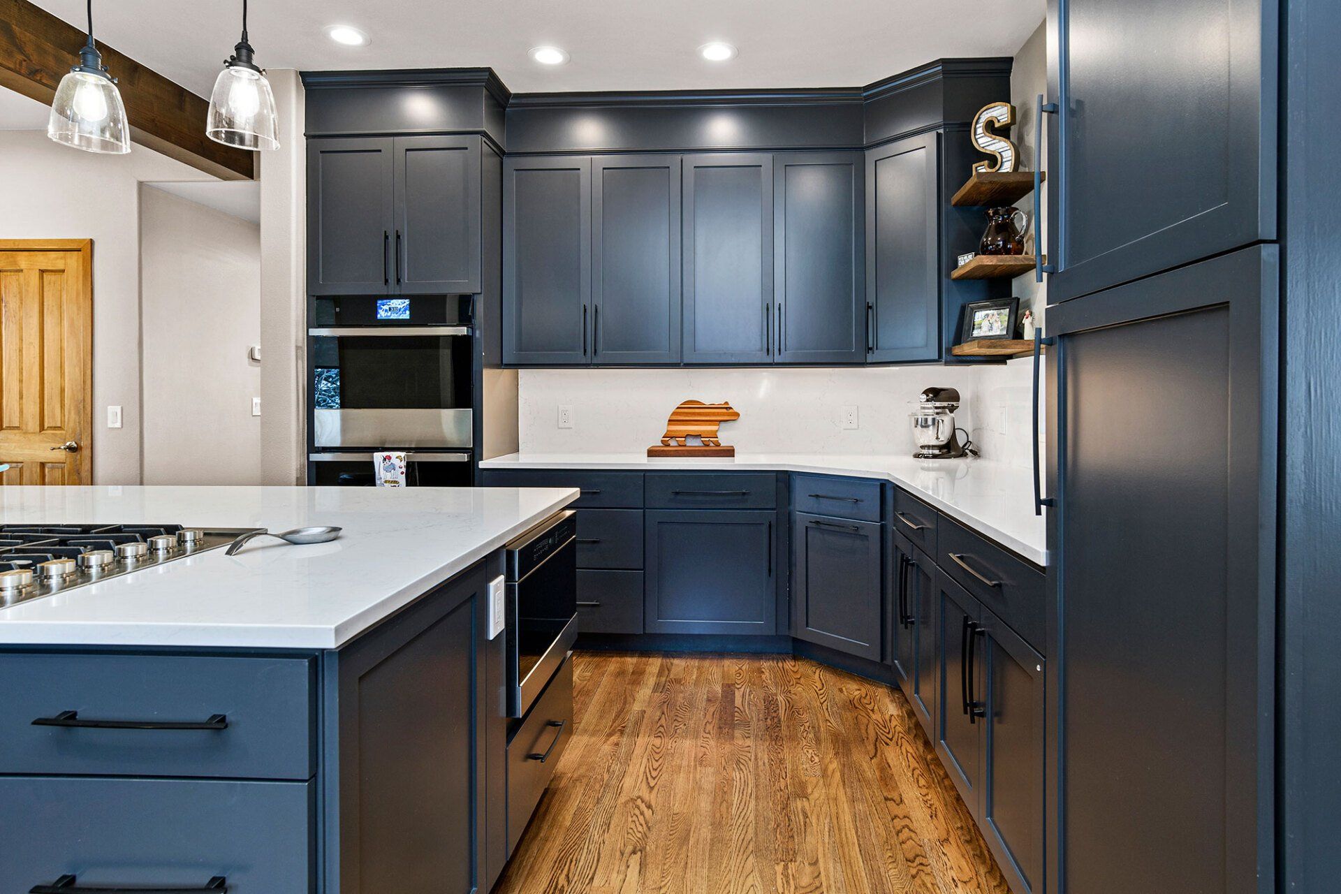 A kitchen with blue cabinets , white counter tops , and stainless steel appliances.