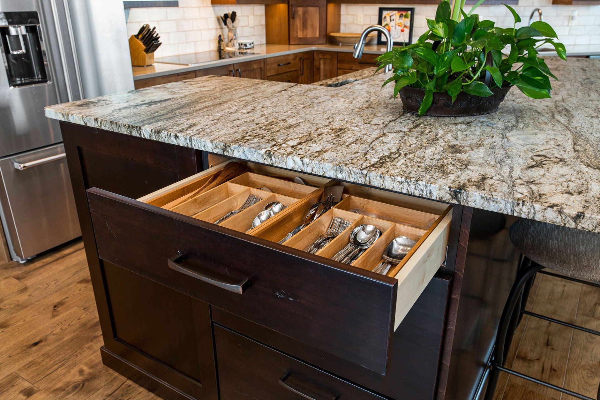 A kitchen with a granite counter top and a wooden drawer filled with silverware.