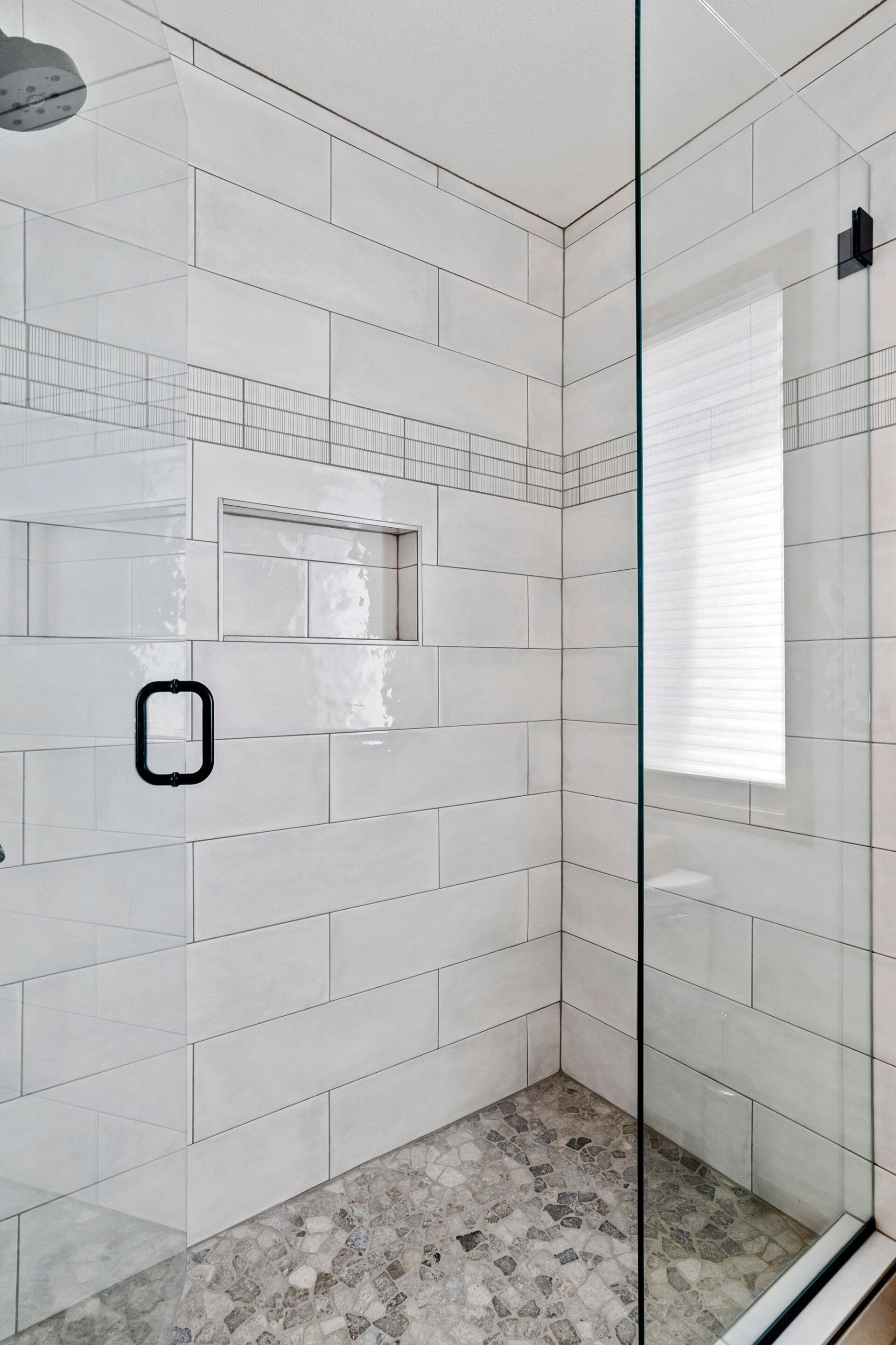 A bathroom with white tiles and a walk in shower with a glass door.