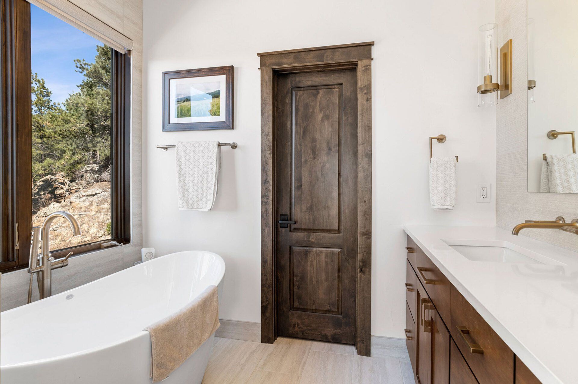 A bathroom with a tub , sink , mirror and window.