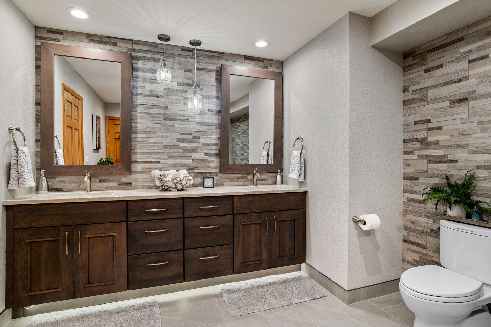 A bathroom with two sinks , two mirrors and a toilet.