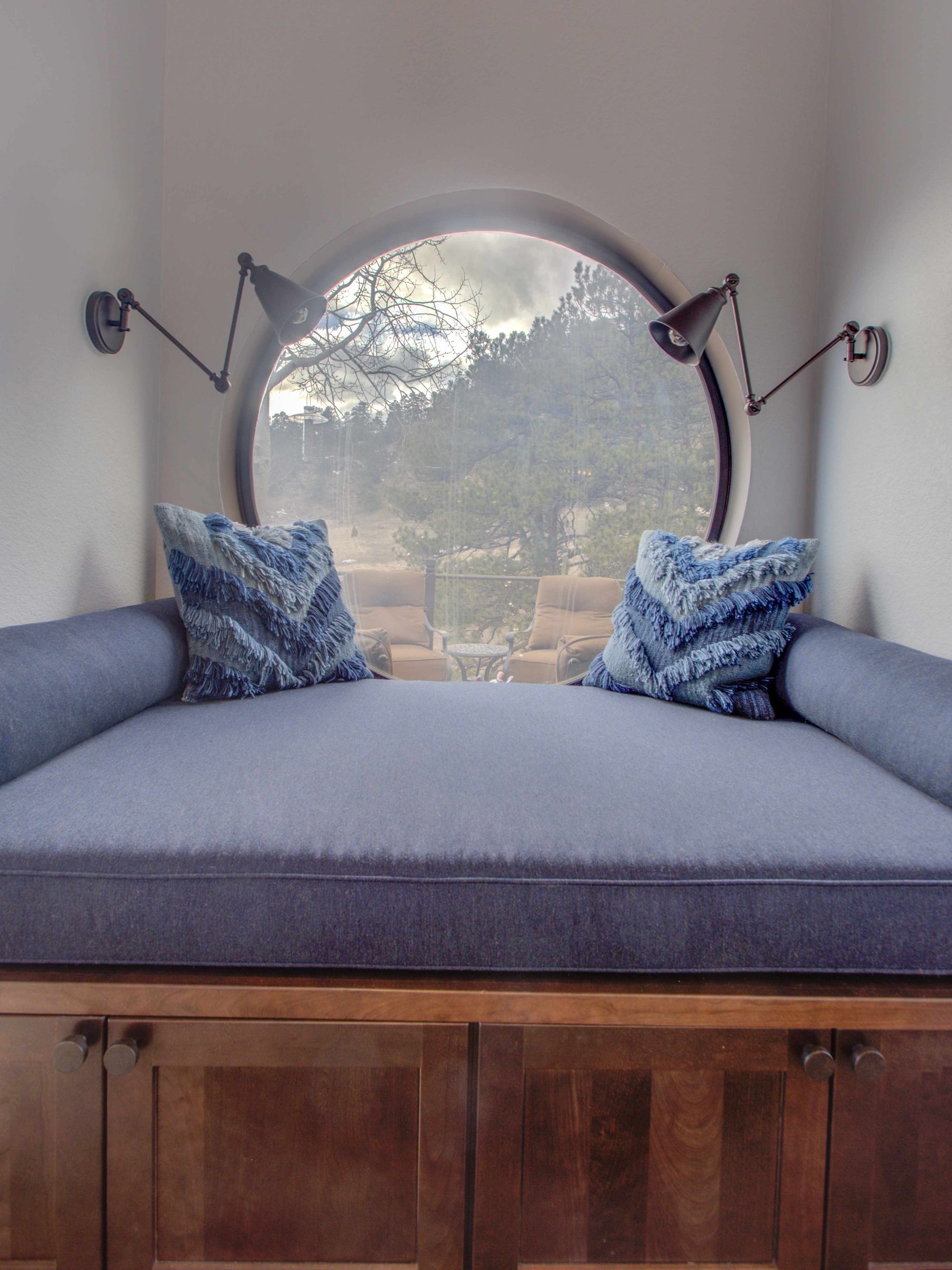 A couch with blue pillows sits in front of a round window