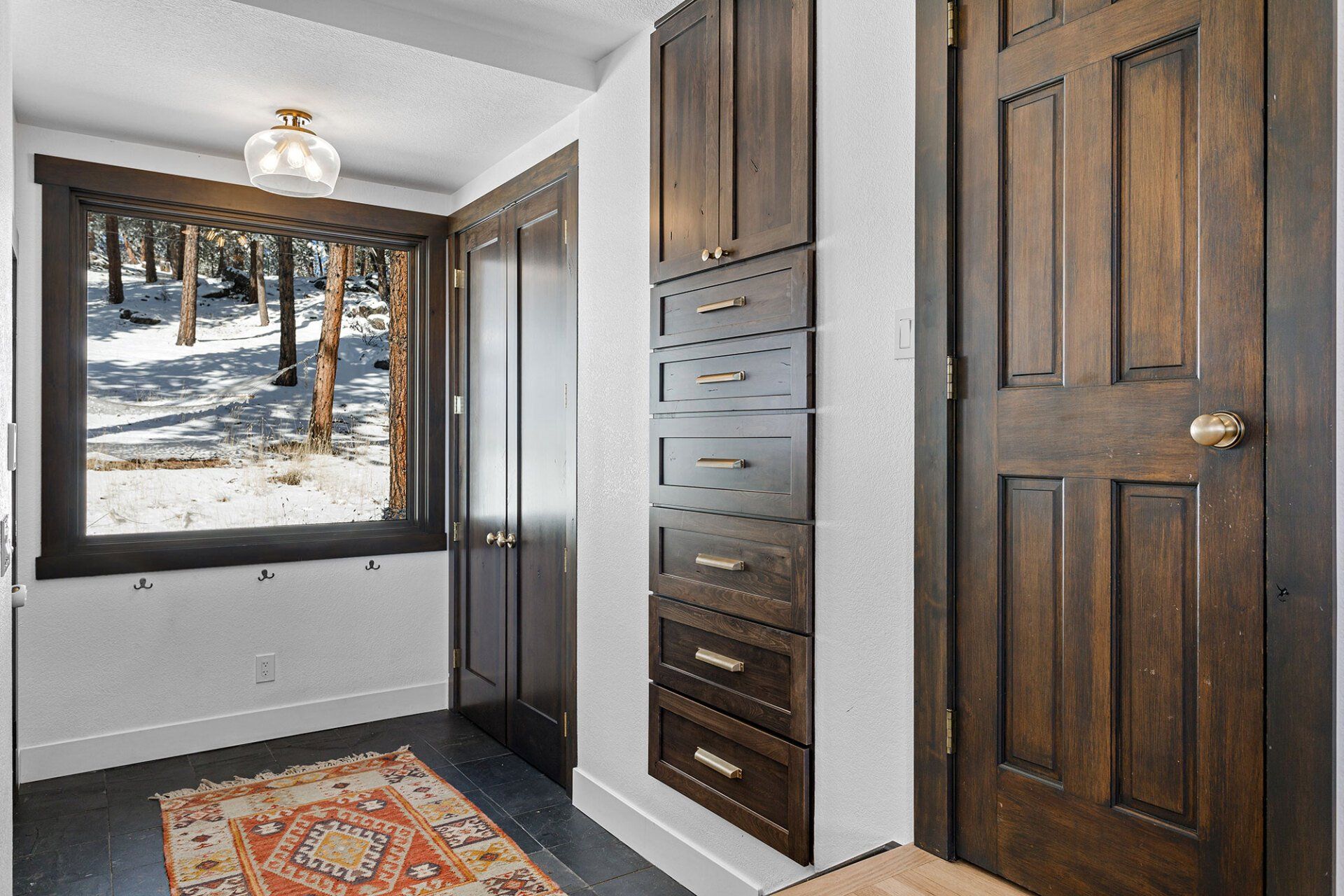 A hallway with wooden doors , drawers , a rug and a window.