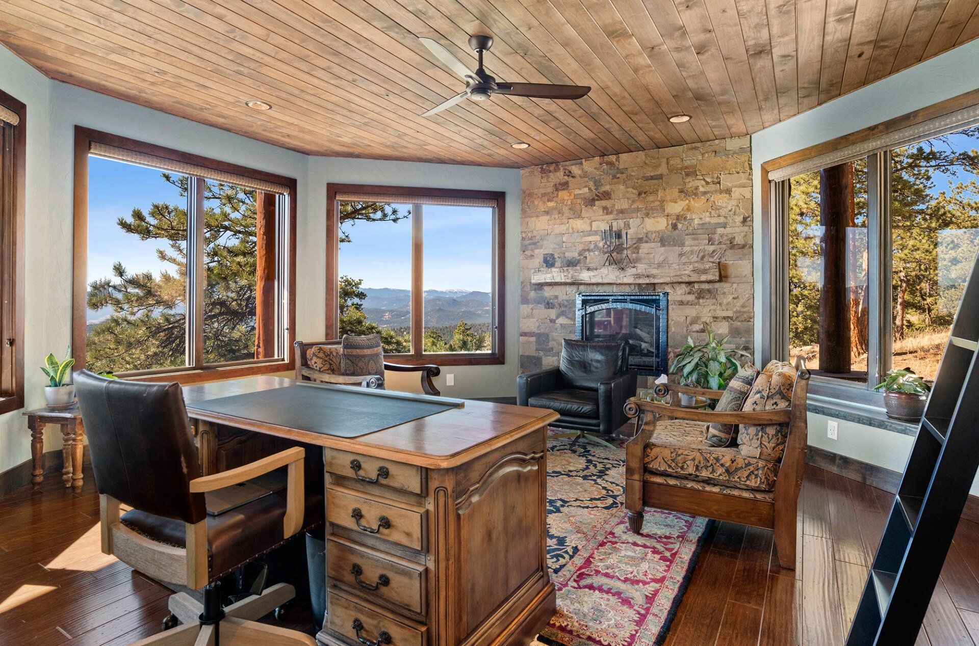 A living room with a desk and chairs and a ceiling fan.