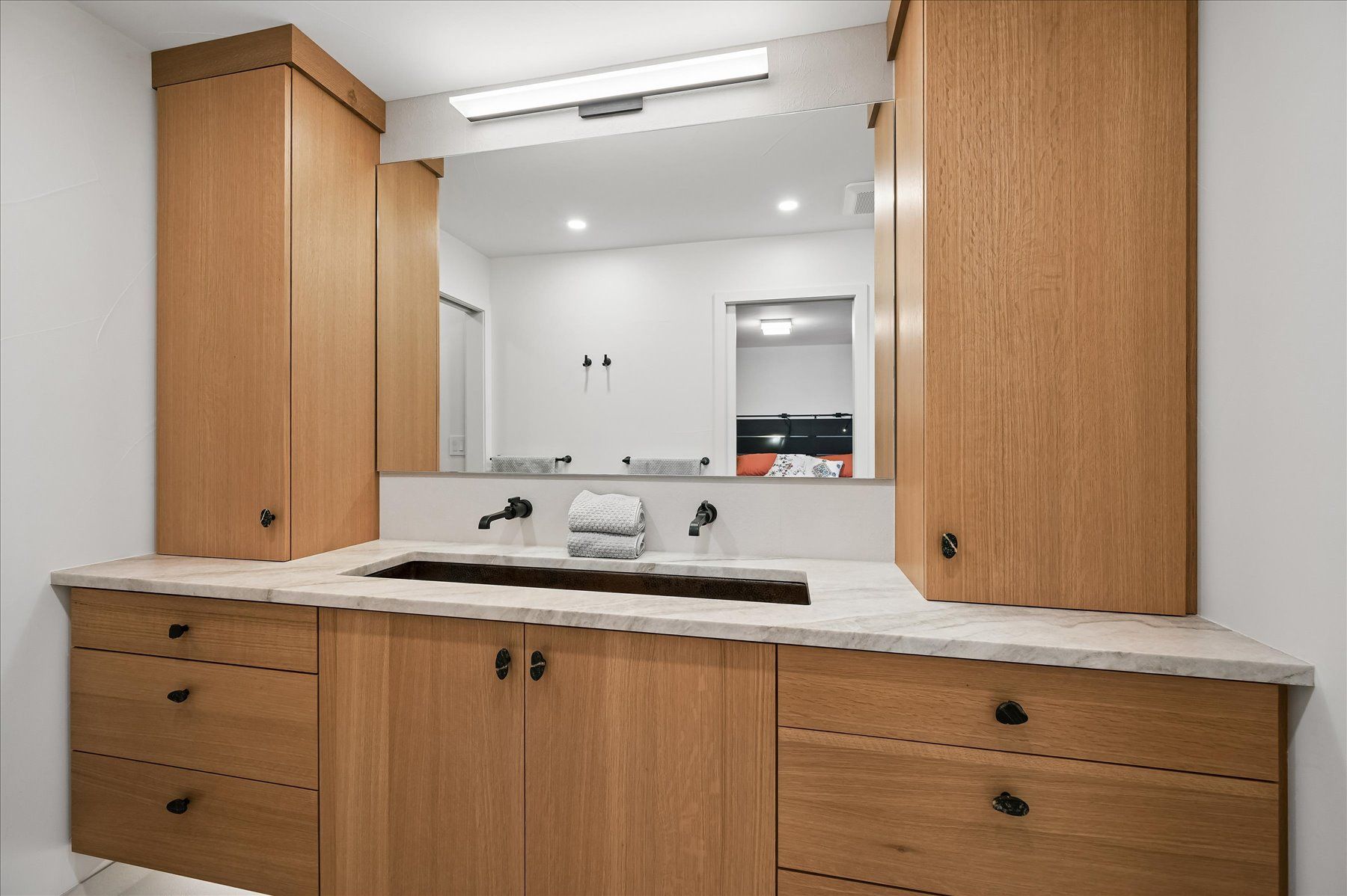 Modern bathroom vanity with wood cabinets, double sinks, and a large mirror with built-in lighting