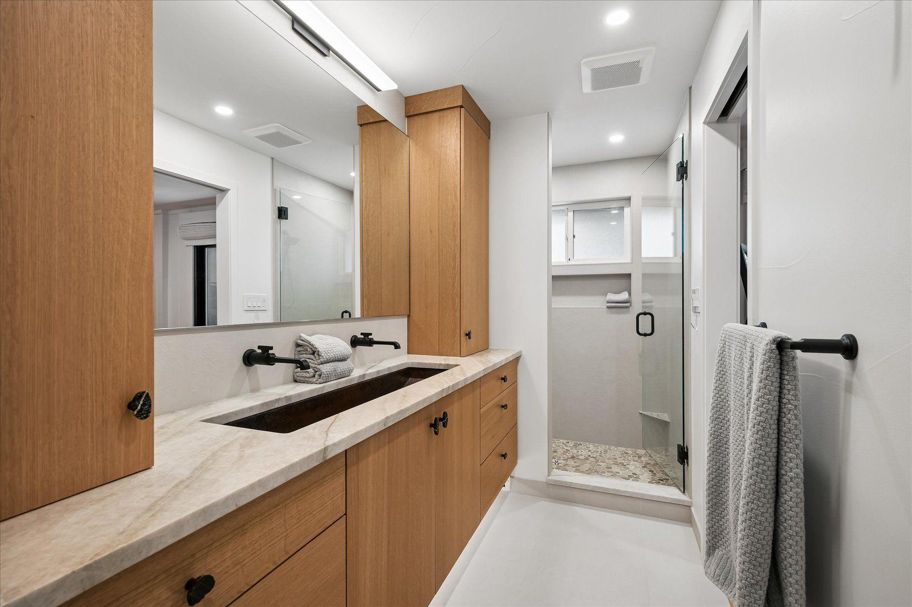 Modern bathroom with double vanity, large mirror, wood cabinets, and tiled shower area
