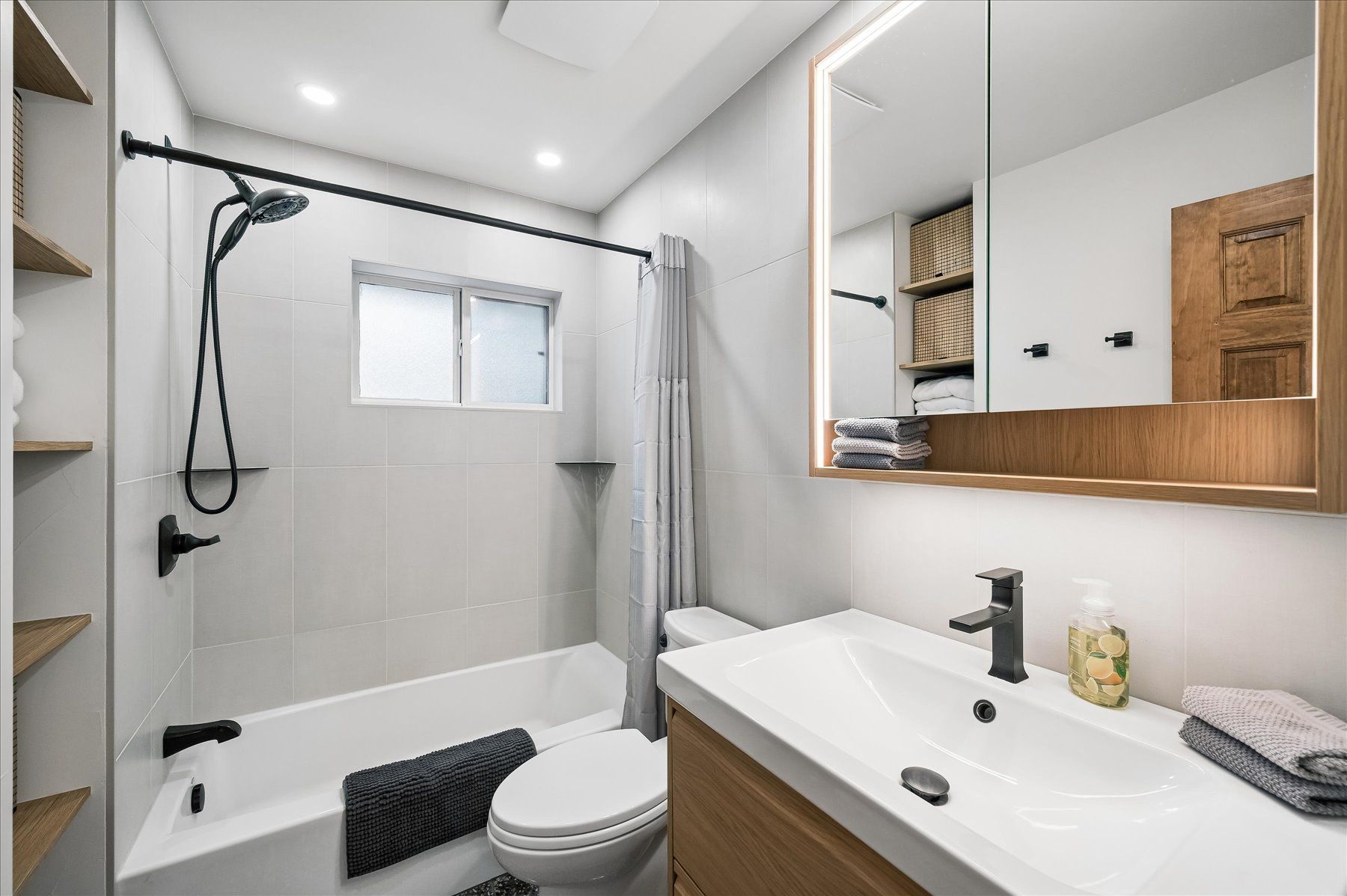 Modern bathroom with walk-in shower, toilet, and white vanity with wood accents