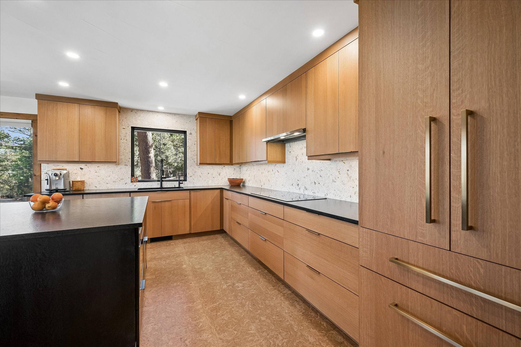 Modern kitchen with light wood cabinets, black island, and large window over the sink.